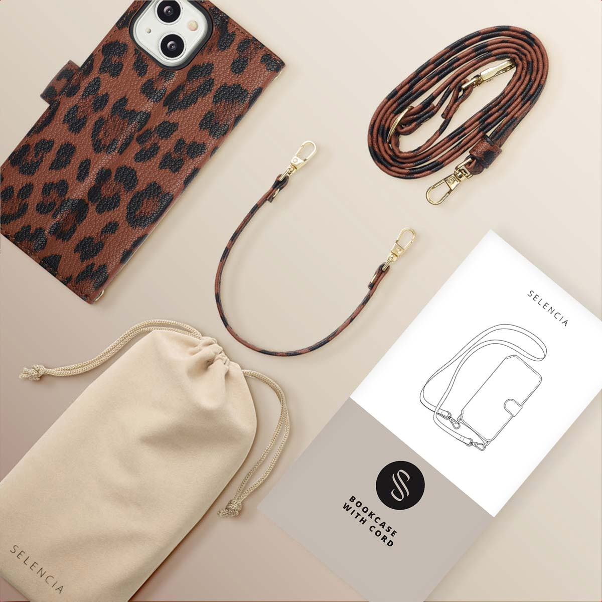 Custodia per telefono con stampa leopardata, cinturino, custodia e manuale su superficie beige. Accessori disposti. Il testo sul manuale dice Selencia.