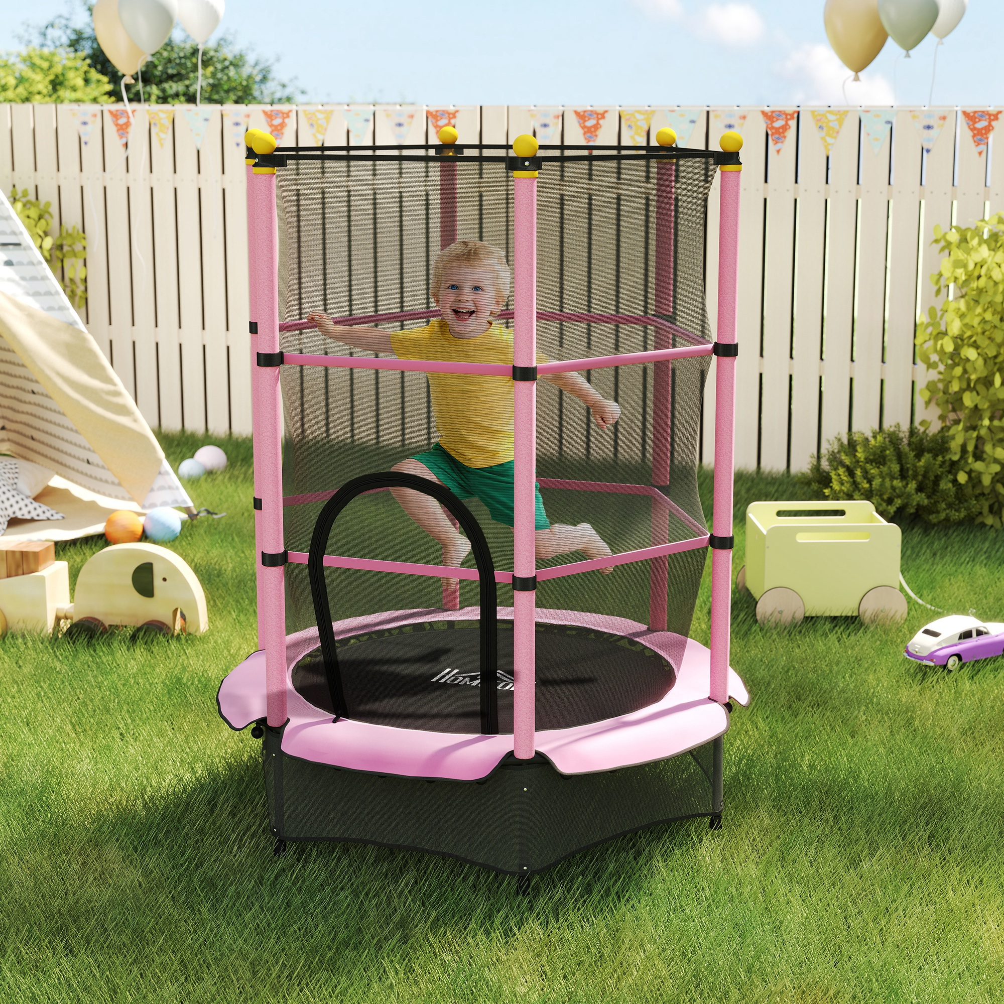 Un bambino salta su un trampolino rosa in un cortile. C'è una recinzione bianca, giocattoli e palloncini sullo sfondo.
