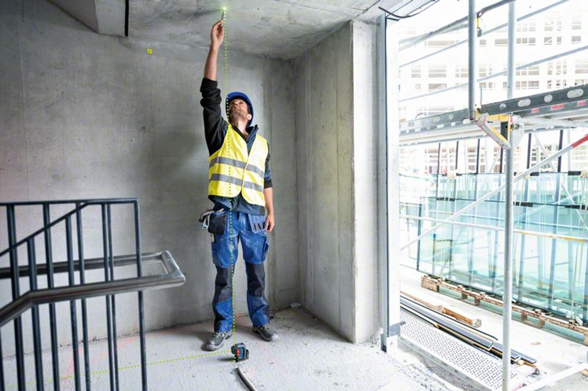 Un trabajador de la construcción con chaleco amarillo y pantalones de trabajo azules usa un nivel láser.