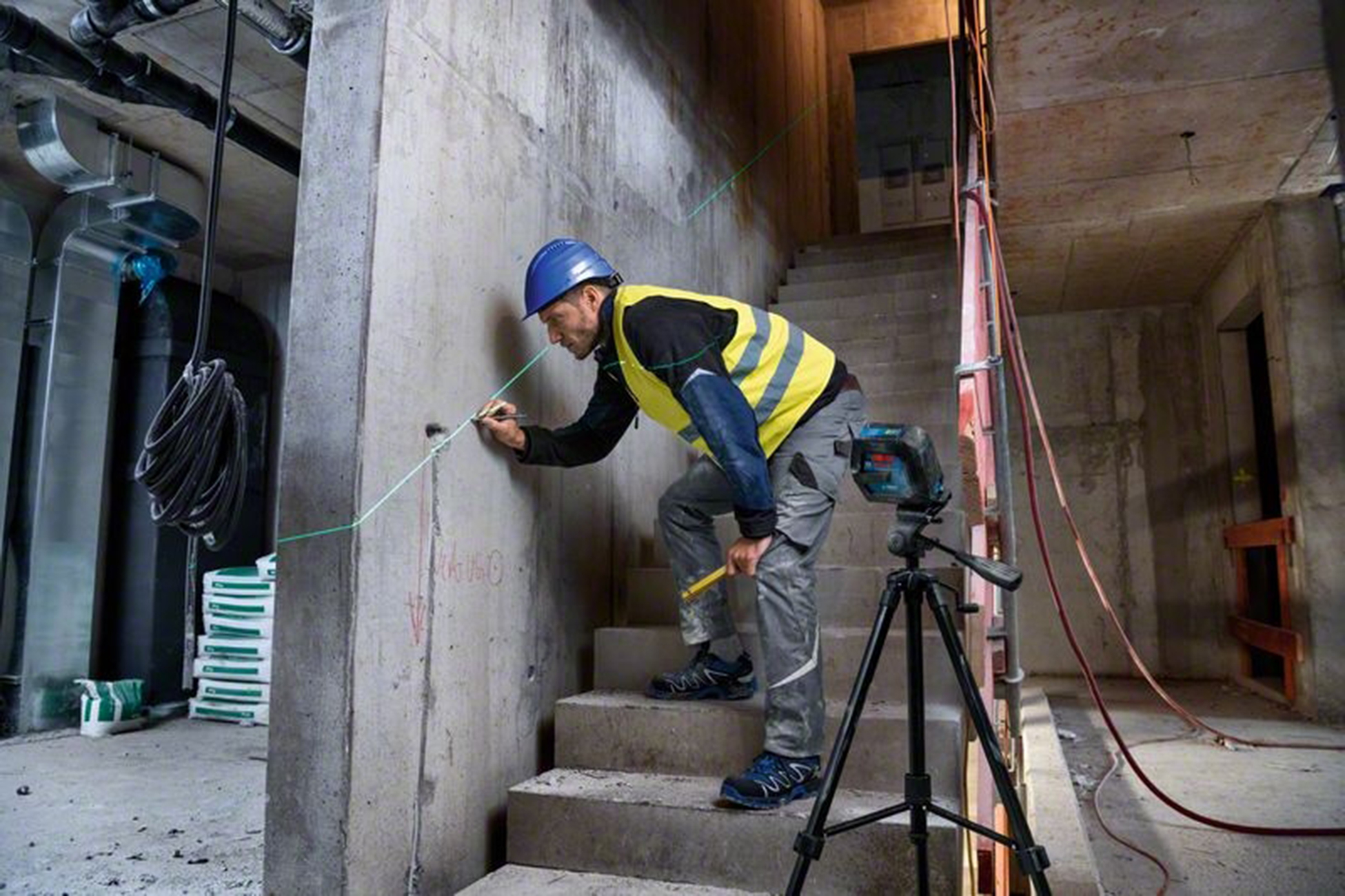 Un operaio con casco e gilet segna un muro.