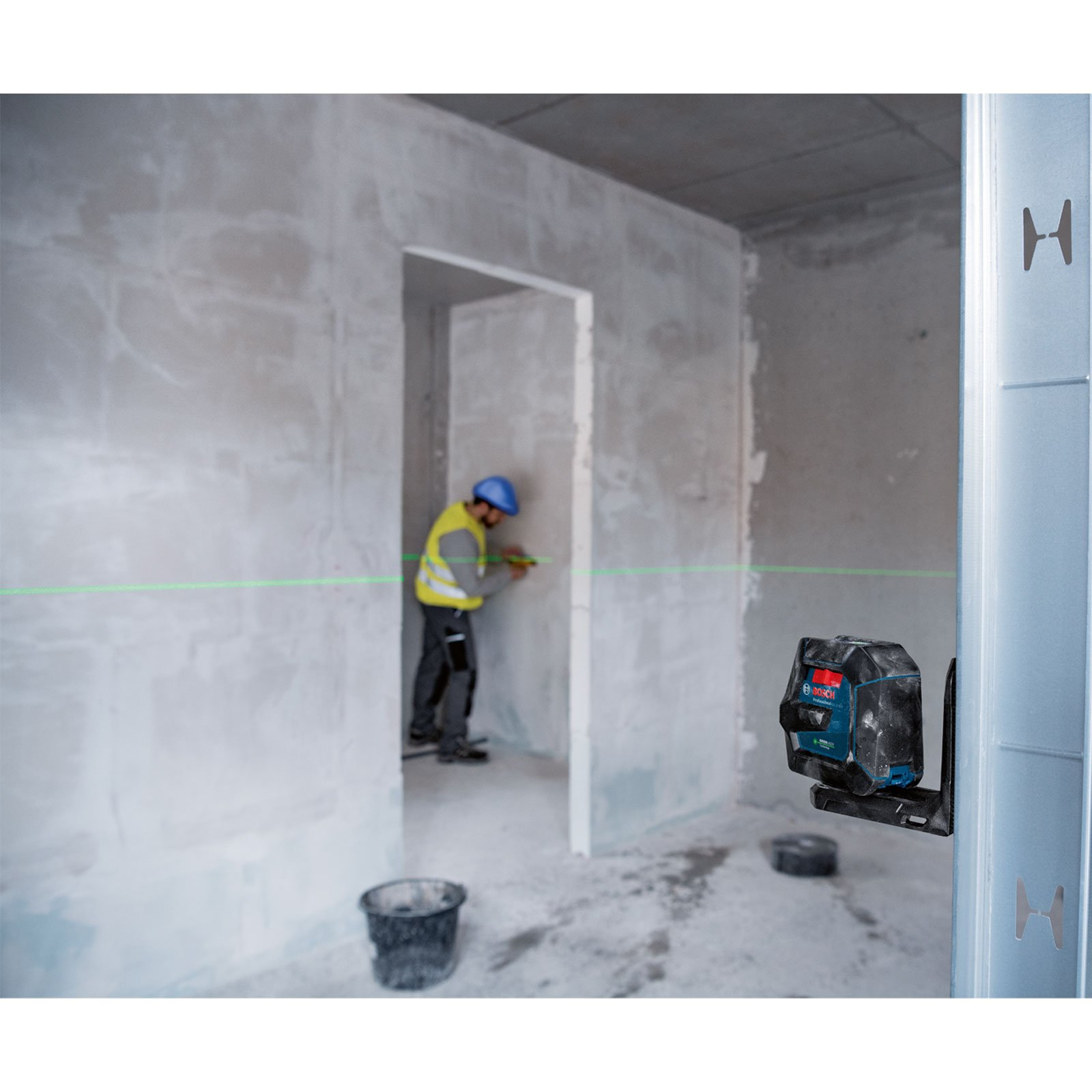 Un operaio edile usa un livello laser. Una linea verde è visibile. La scena è all'interno di un edificio in costruzione.