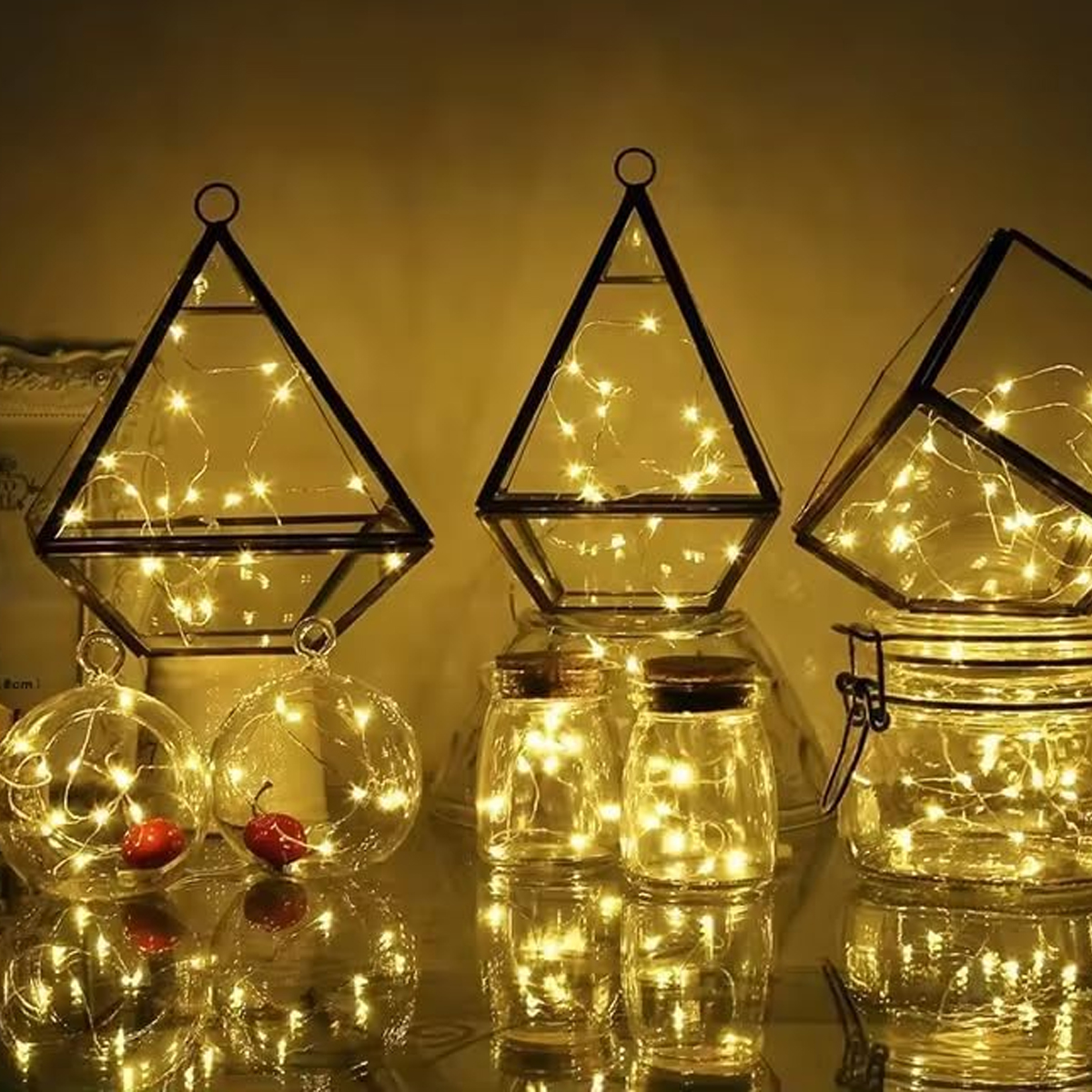 Gläserne Laternen und Gläser gefüllt mit Lichterketten. Enthält geometrische Terrarien, runde Glasornamente und Gläser mit Holzdeckeln.