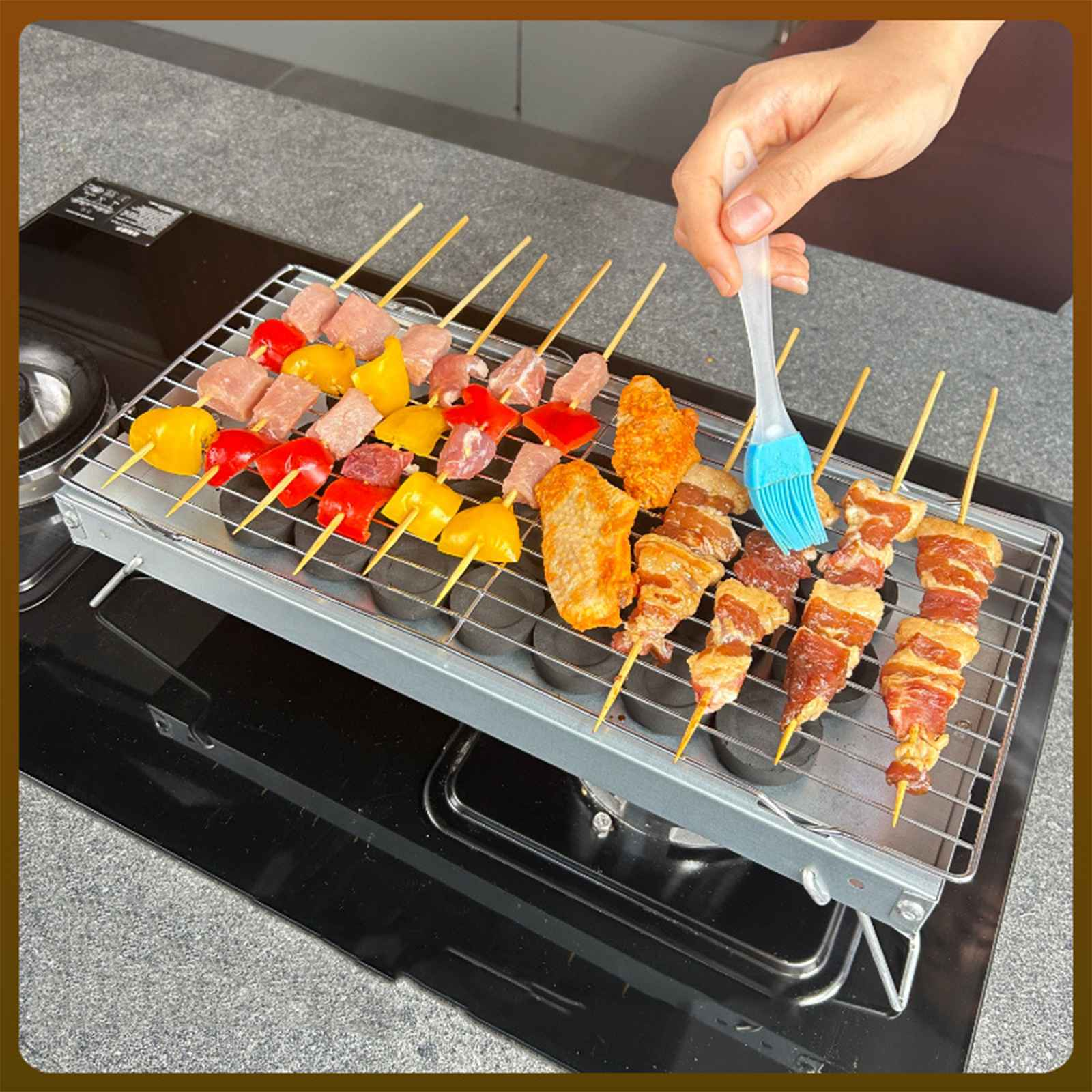 Auf einem Grill aufgespießtes Fleisch und Gemüse. Eine Hand bestreicht das Essen mit einem blauen Pinsel. Schwarzes Kochfeld im Hintergrund.