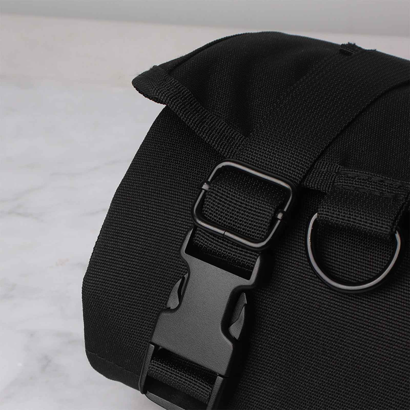 Nahaufnahme einer schwarzen Stofftasche mit Schnalle und D-Ring. Der Hintergrund ist eine helle Marmoroberfläche.