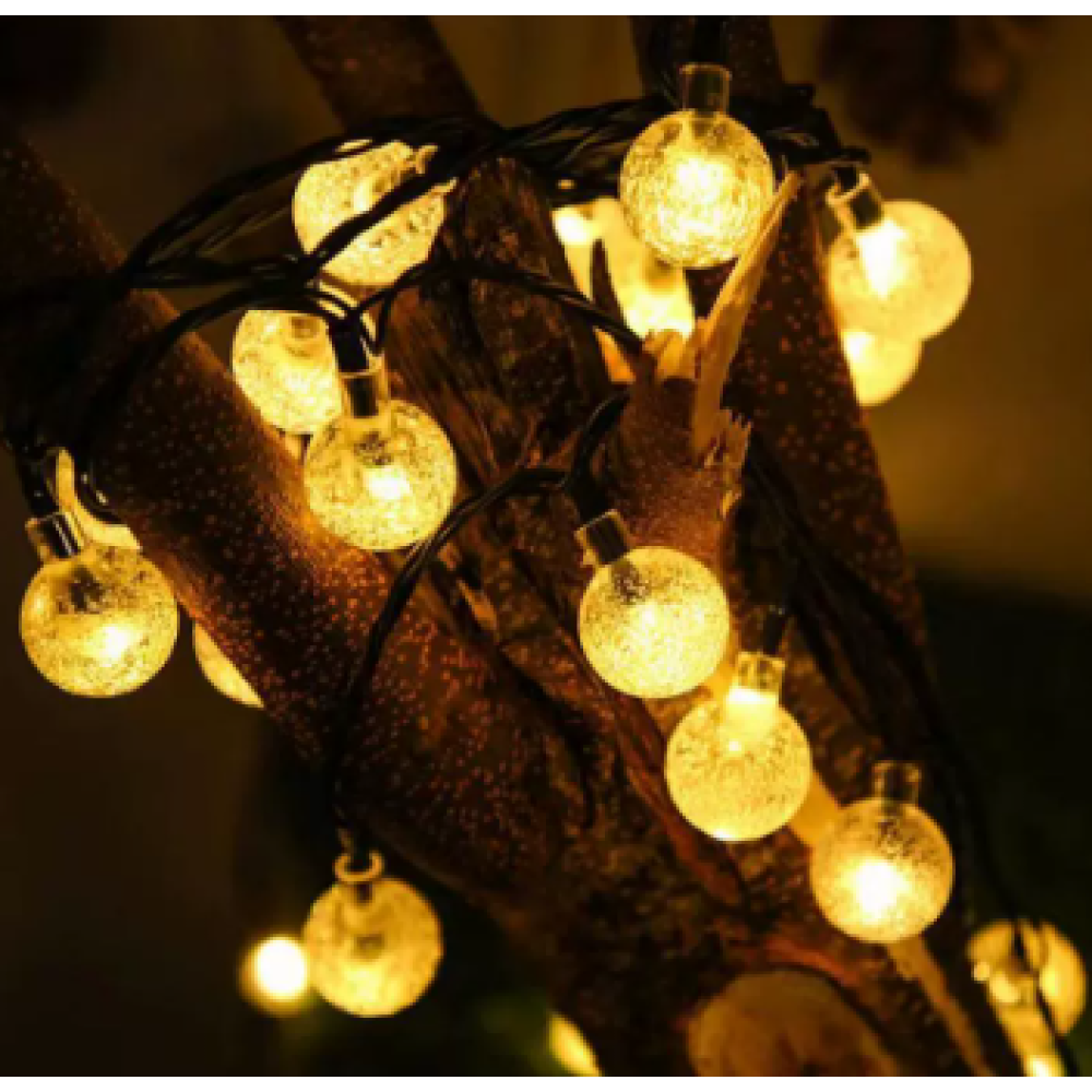 Lichterketten mit runden Glühbirnen sind an einem Ast befestigt. Die Lichter leuchten gelb vor dunklem Hintergrund.