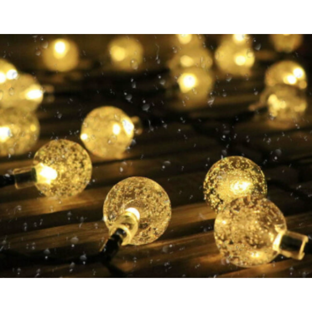 Nahaufnahme von Lichterketten mit Glaskugeln. Sie leuchten golden und einige Wassertropfen sind sichtbar.