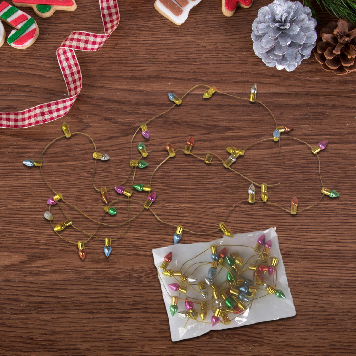 Draufsicht auf Weihnachtsbeleuchtung auf einem Holztisch mit Keksen, Schleife, Tannenzapfen und einer silbernen Tannenzapfendekoration.