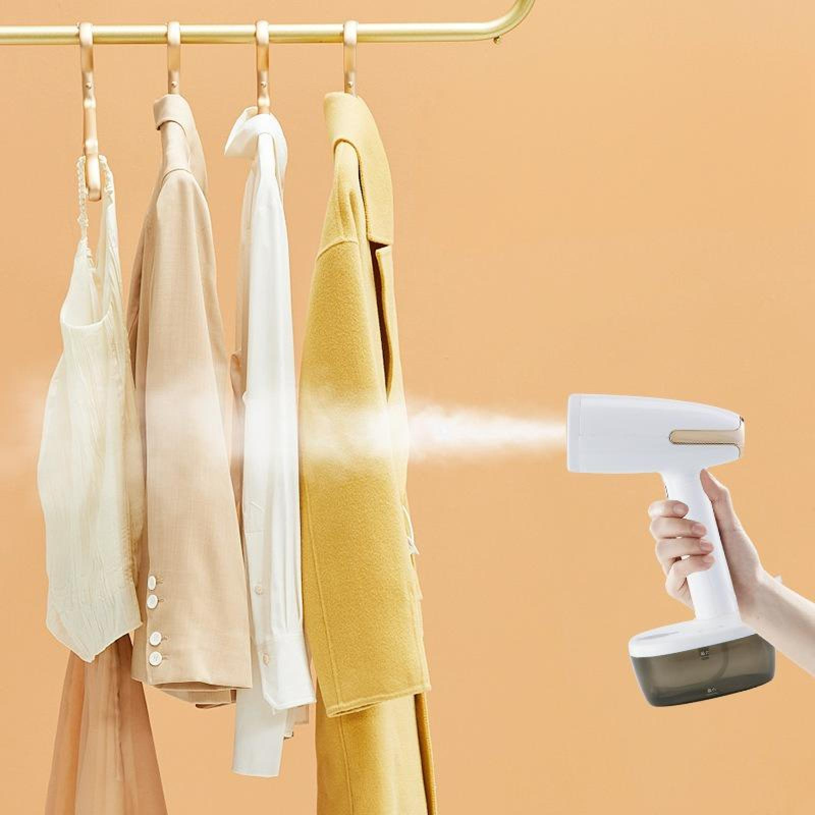 Eine Hand dämpft Kleidung mit einem weißen Steamer. Kleidung hängt an einem goldenen Gestell. Der Hintergrund ist orange.