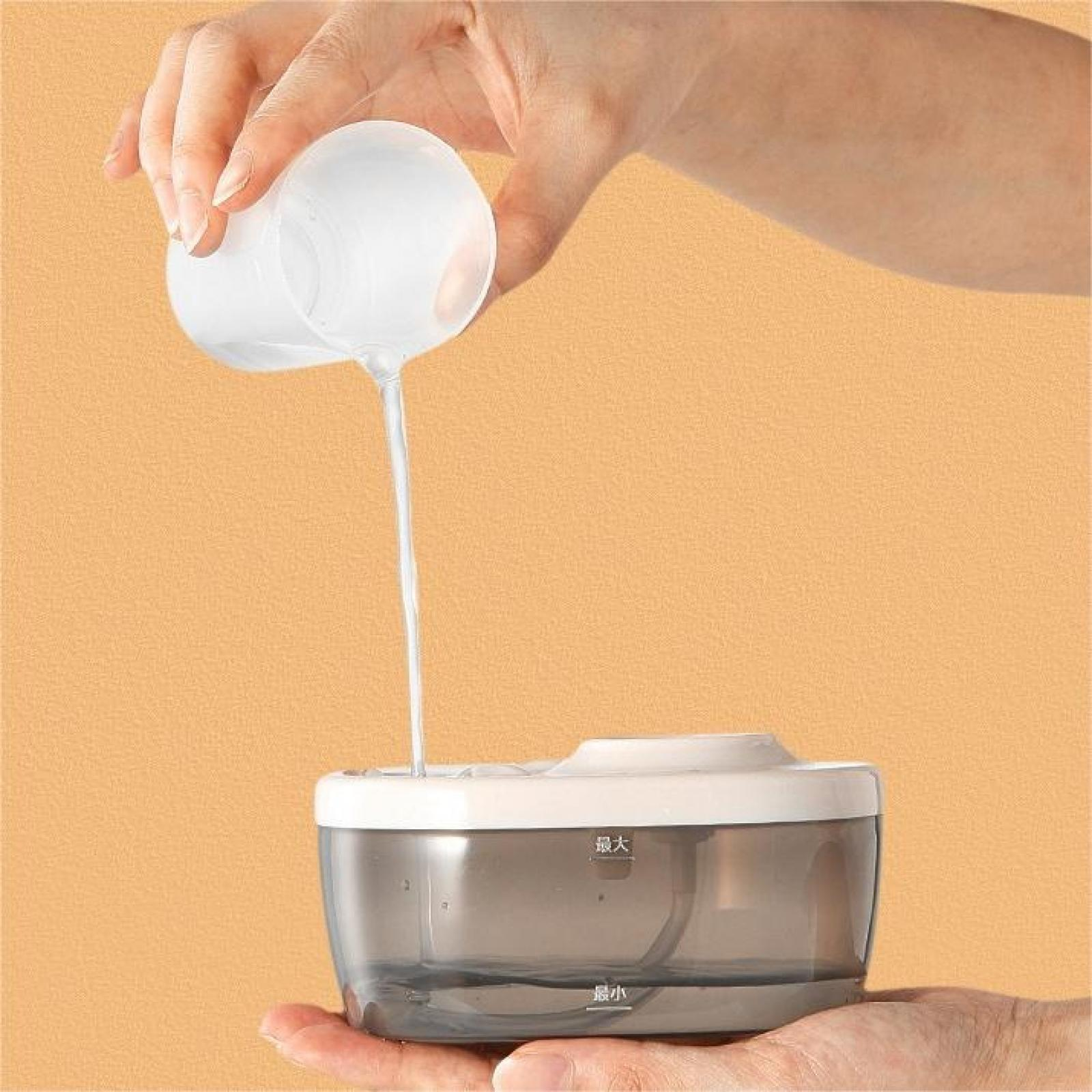 Eine Hand gießt Wasser aus einem weißen Becher in einen transparenten Behälter mit weißem Deckel. Der Hintergrund ist orange.