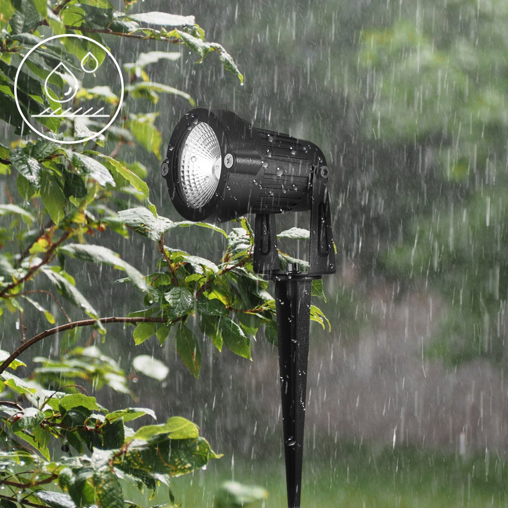 Ein schwarzer Scheinwerfer im Regen. Grüne Blätter im Vordergrund. Regentropfen fallen. Ein wasserdichtes Symbol befindet sich oben links.