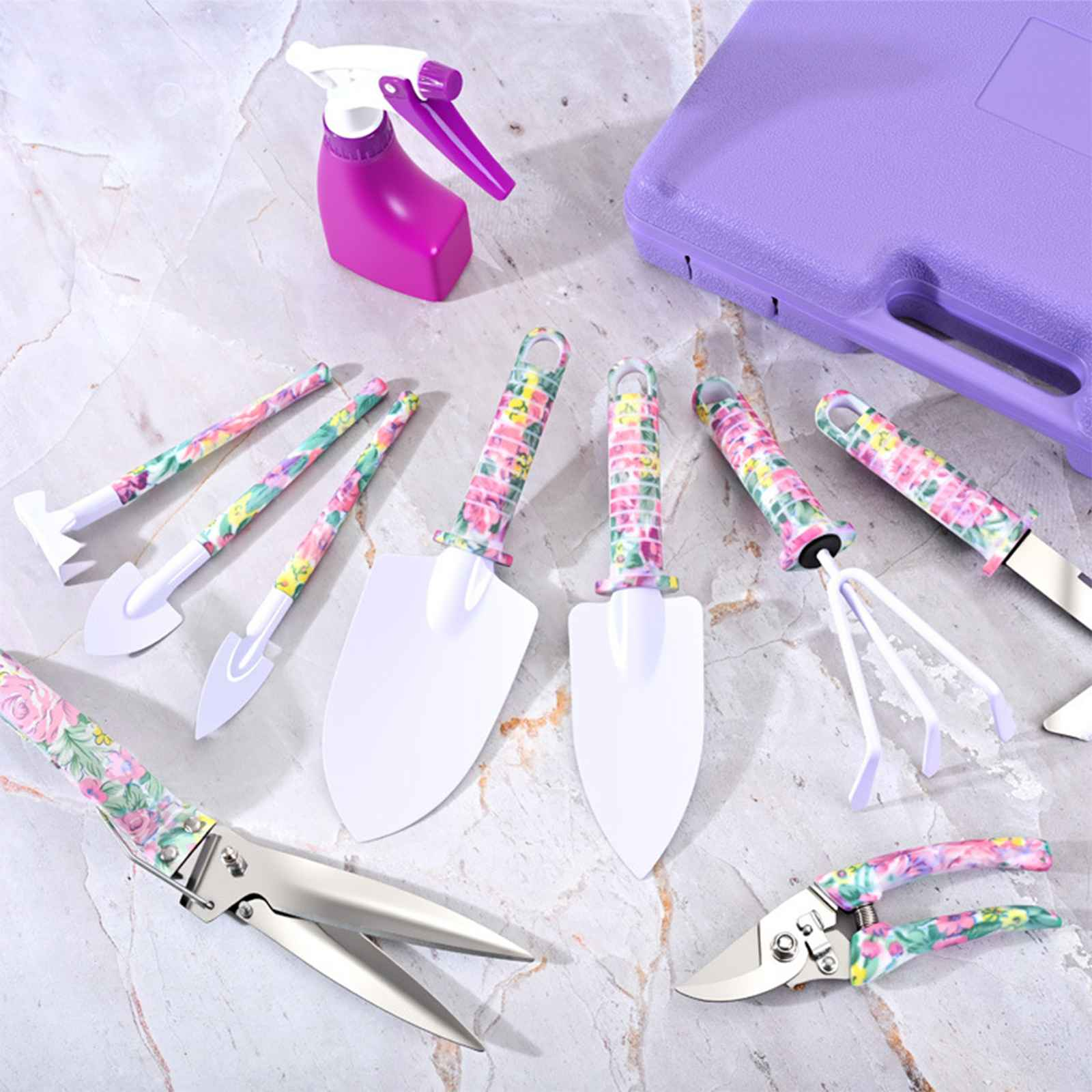 Gartengeräte-Set mit Blumenmustern. Enthält Spaten, Scheren, Sprühflasche und einen lila Koffer, angeordnet auf Marmor.