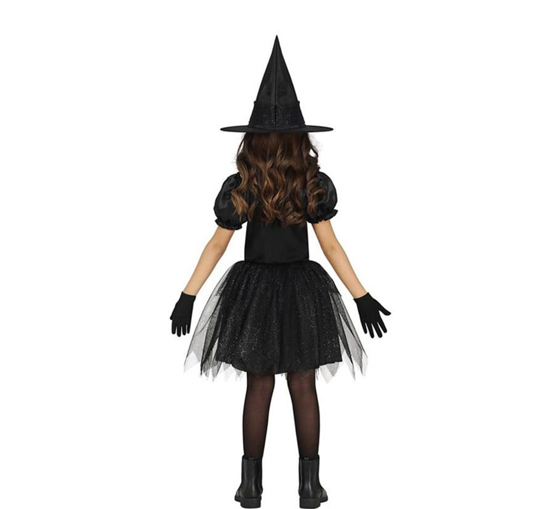 Una niña de espaldas vestida con un disfraz de bruja negro, que incluye sombrero, vestido, guantes y botas, sobre un fondo blanco.