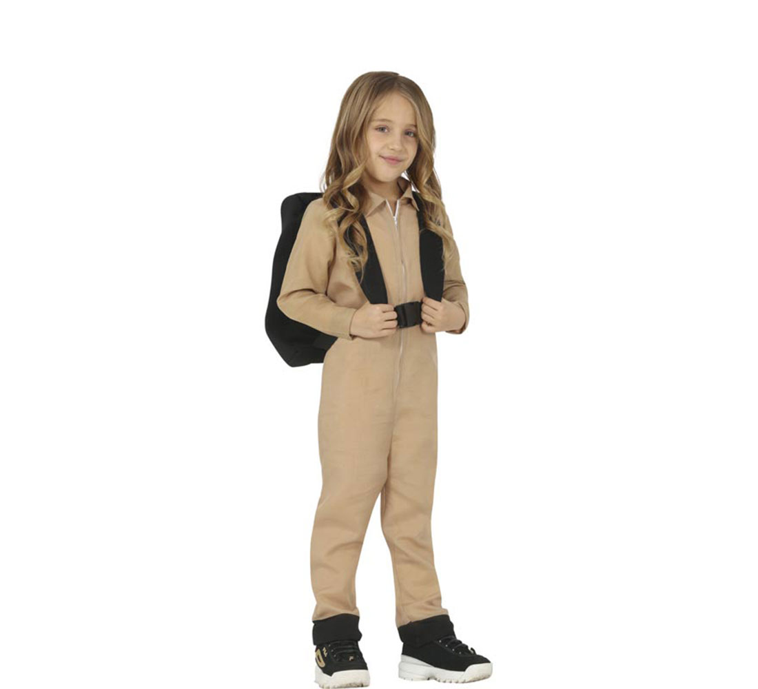 Una niña está de pie con un mono color beige, una mochila negra y zapatillas deportivas. Sonríe mirando al espectador sobre un fondo blanco.