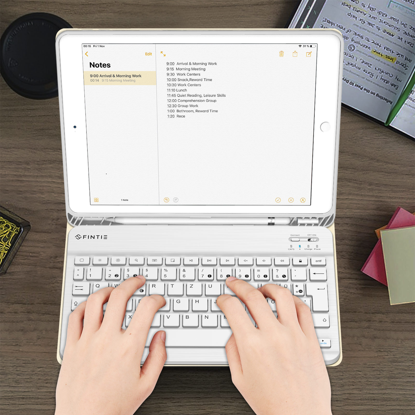 Eine Person, die auf einer Tastatur tippt, die an ein Tablet angeschlossen ist und einen Zeitplan anzeigt. Die Szene befindet sich auf einer Holzoberfläche.