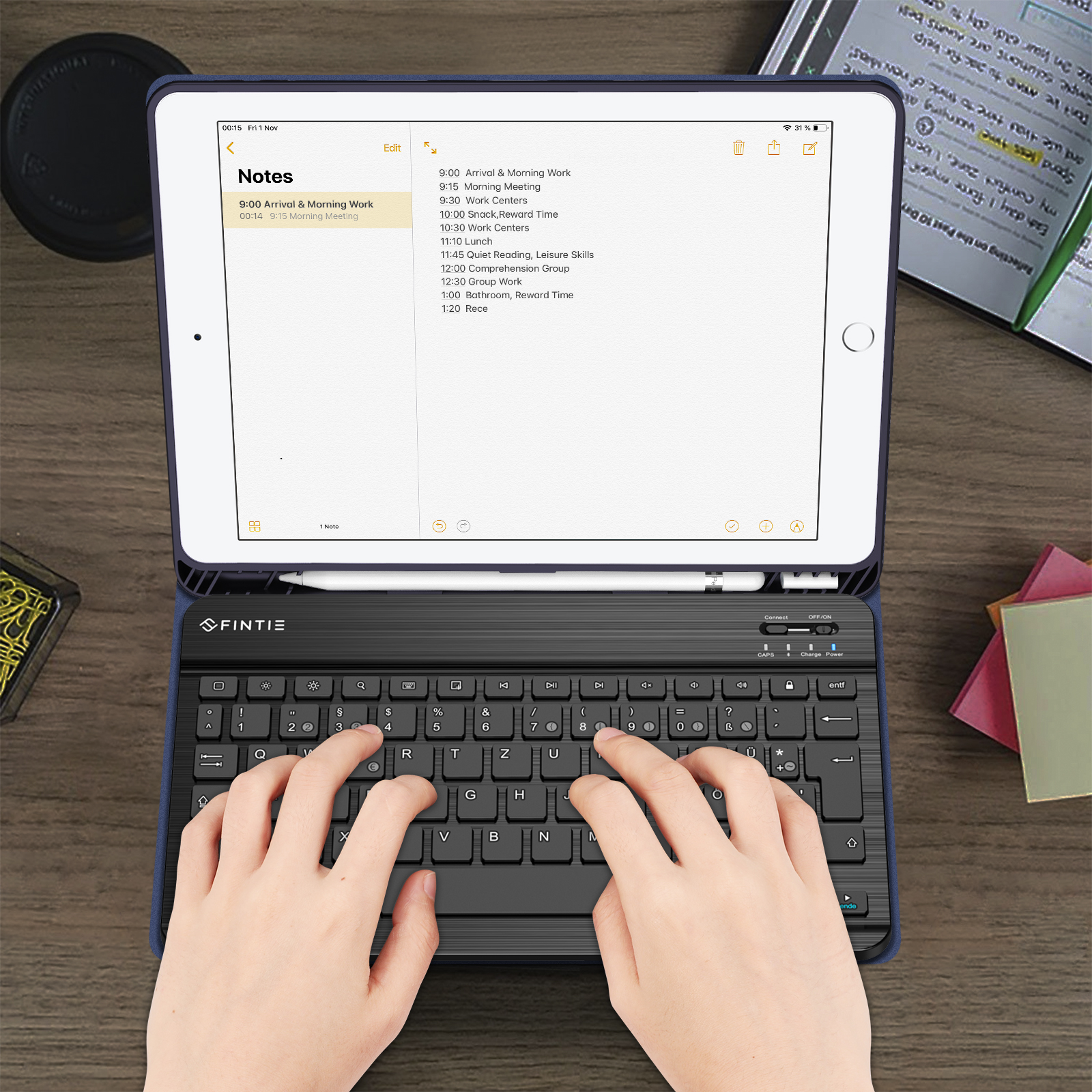 Hände, die auf einer schwarzen Tastatur tippen, die mit einem Tablet verbunden ist, das einen Zeitplan anzeigt. Der Hintergrund ist ein Holztisch.