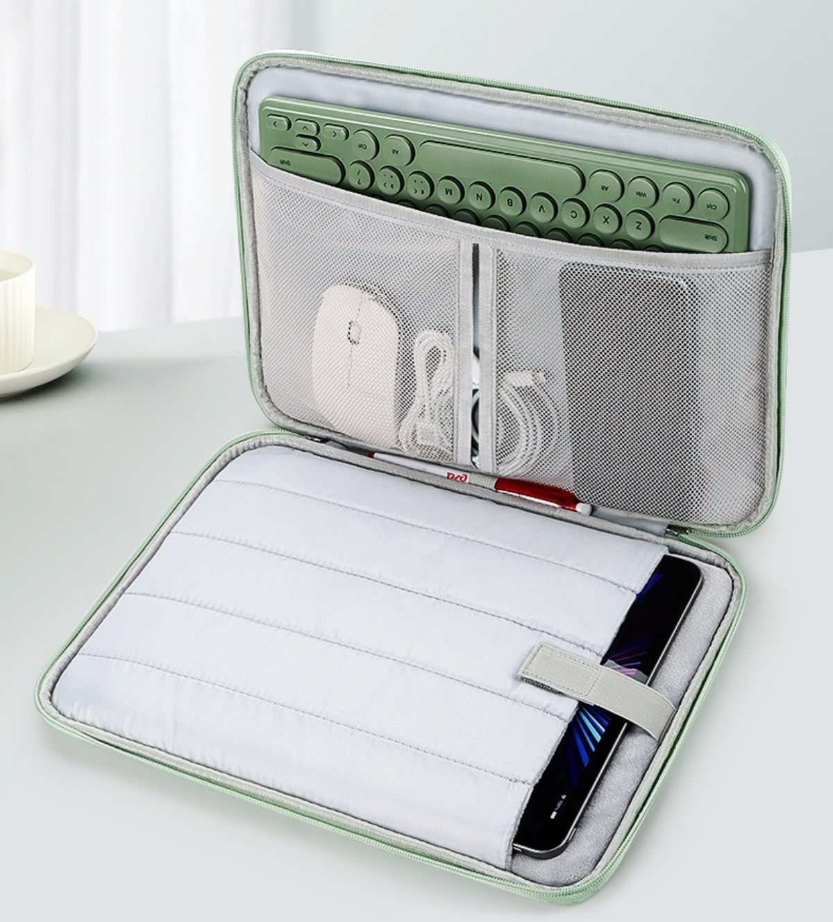 Offene Laptoptasche mit Tastatur, Maus, Tablet und Zubehör. Hellgrüne Tasche auf weißer Oberfläche.
