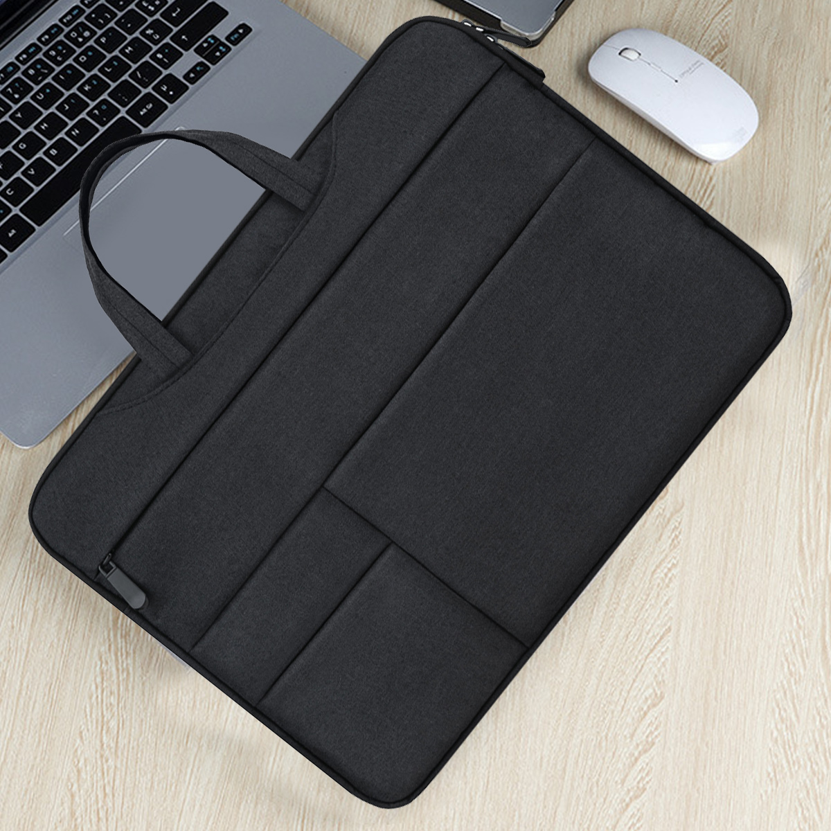 Eine schwarze Laptoptasche mit Griff liegt auf einem Holztisch, ein Laptop, eine Maus und ein Telefon sind ebenfalls sichtbar.