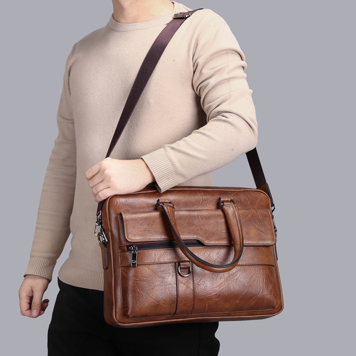 Ein Mann trägt eine braune Ledertasche. Er trägt einen beigen Pullover und eine schwarze Hose. Der Riemen ist braun.