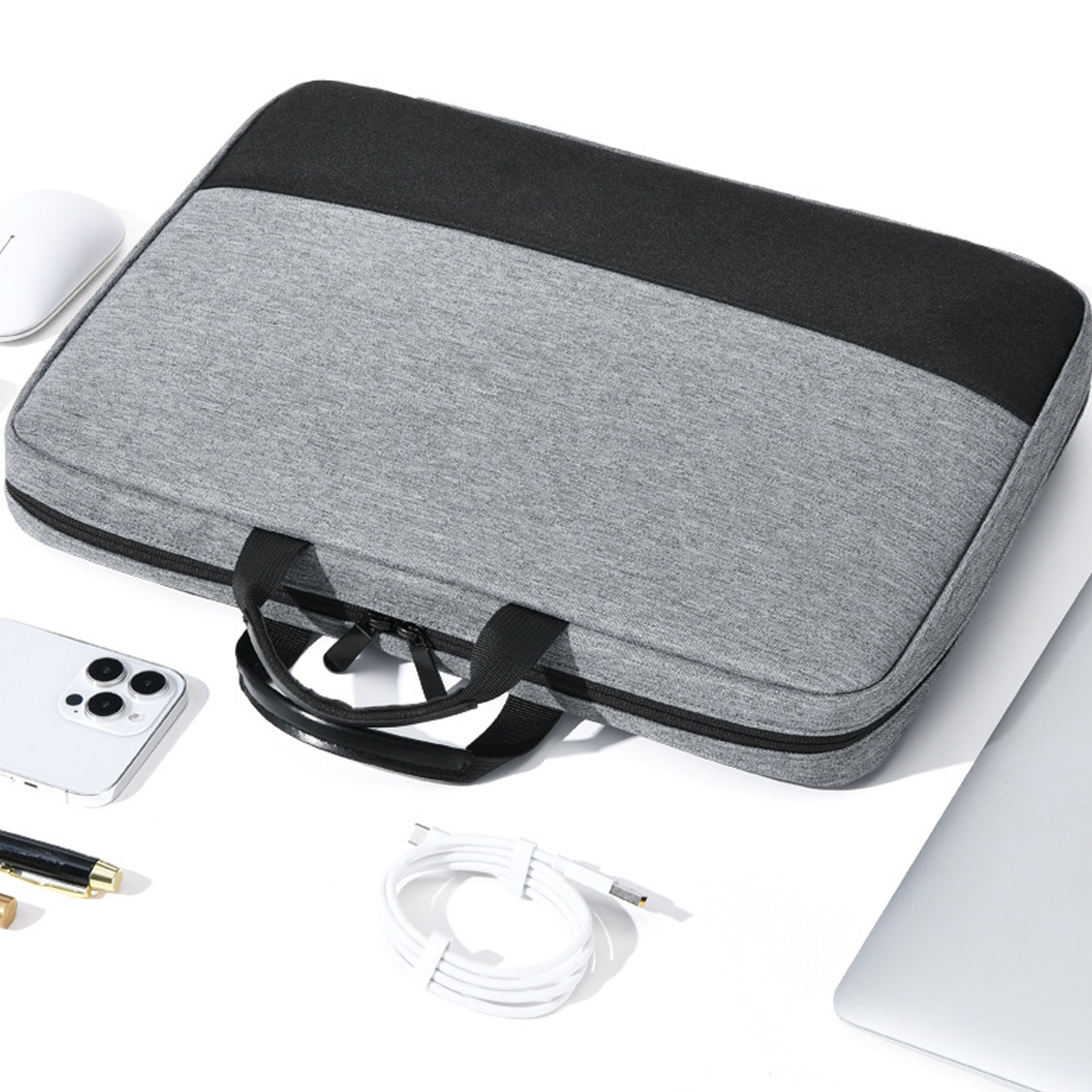 Eine graue Laptoptasche mit schwarzen Akzenten, eine weiße Maus, ein Telefon, ein Stift, ein Kabel und ein Laptop liegen auf einer weißen Oberfläche.