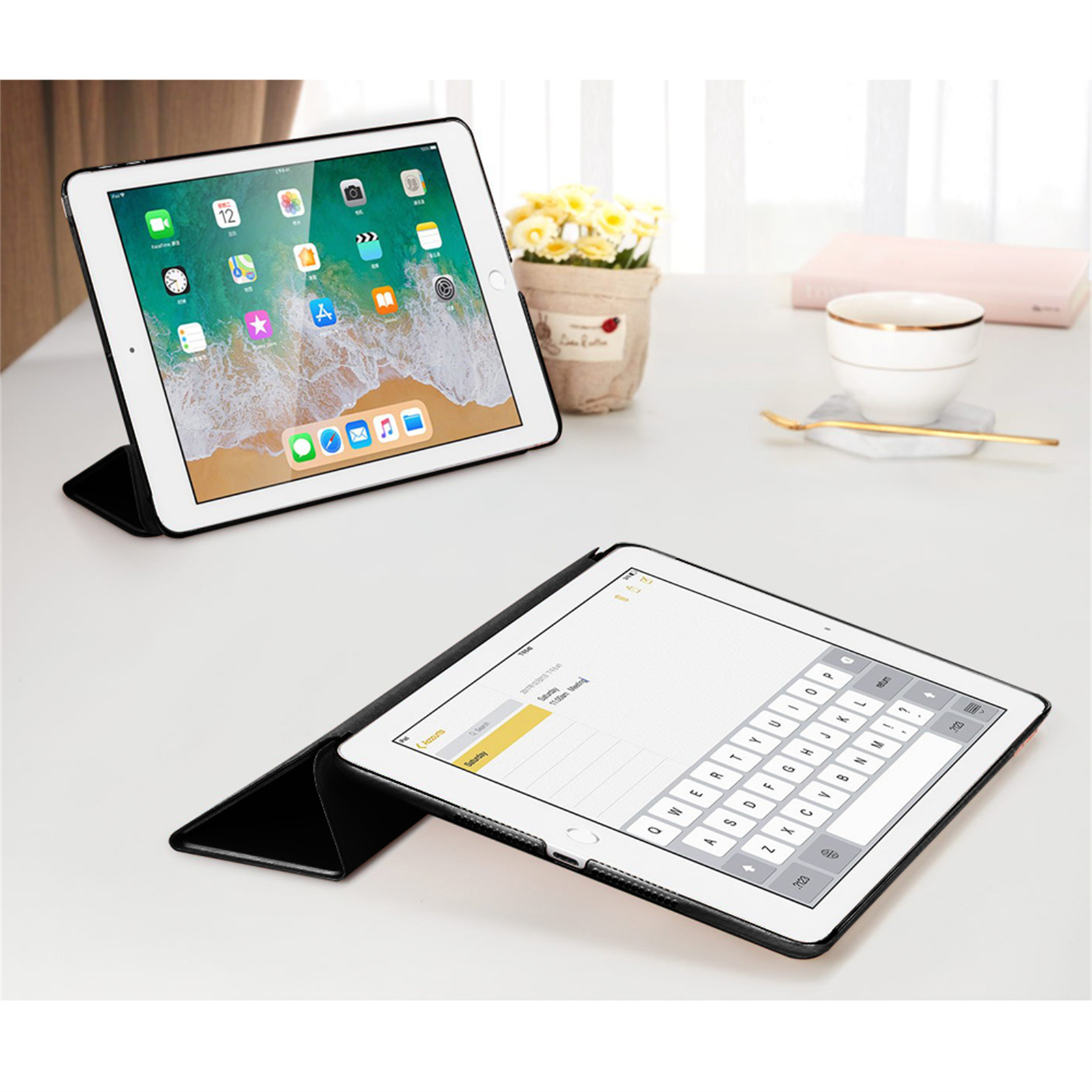 Zwei iPads auf einem weißen Schreibtisch. Eines steht aufrecht und zeigt Apps. Das andere ist mit Tastatur geöffnet. Blumen und Tasse im Hintergrund.