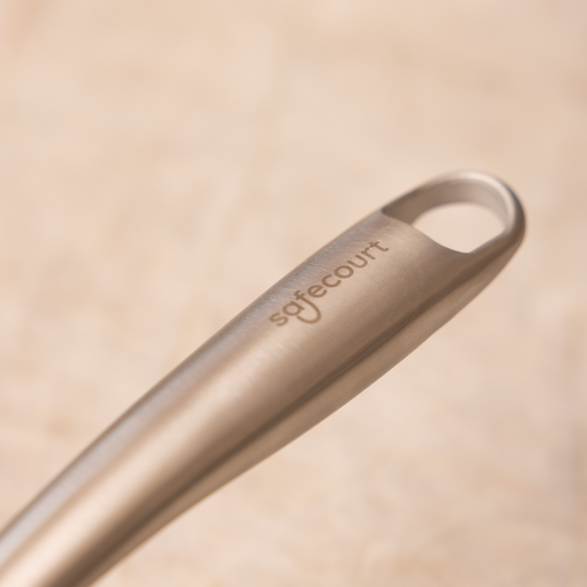 Close-up of a stainless steel handle with a loop, 'safecourt' is engraved on it. Background is blurry beige.