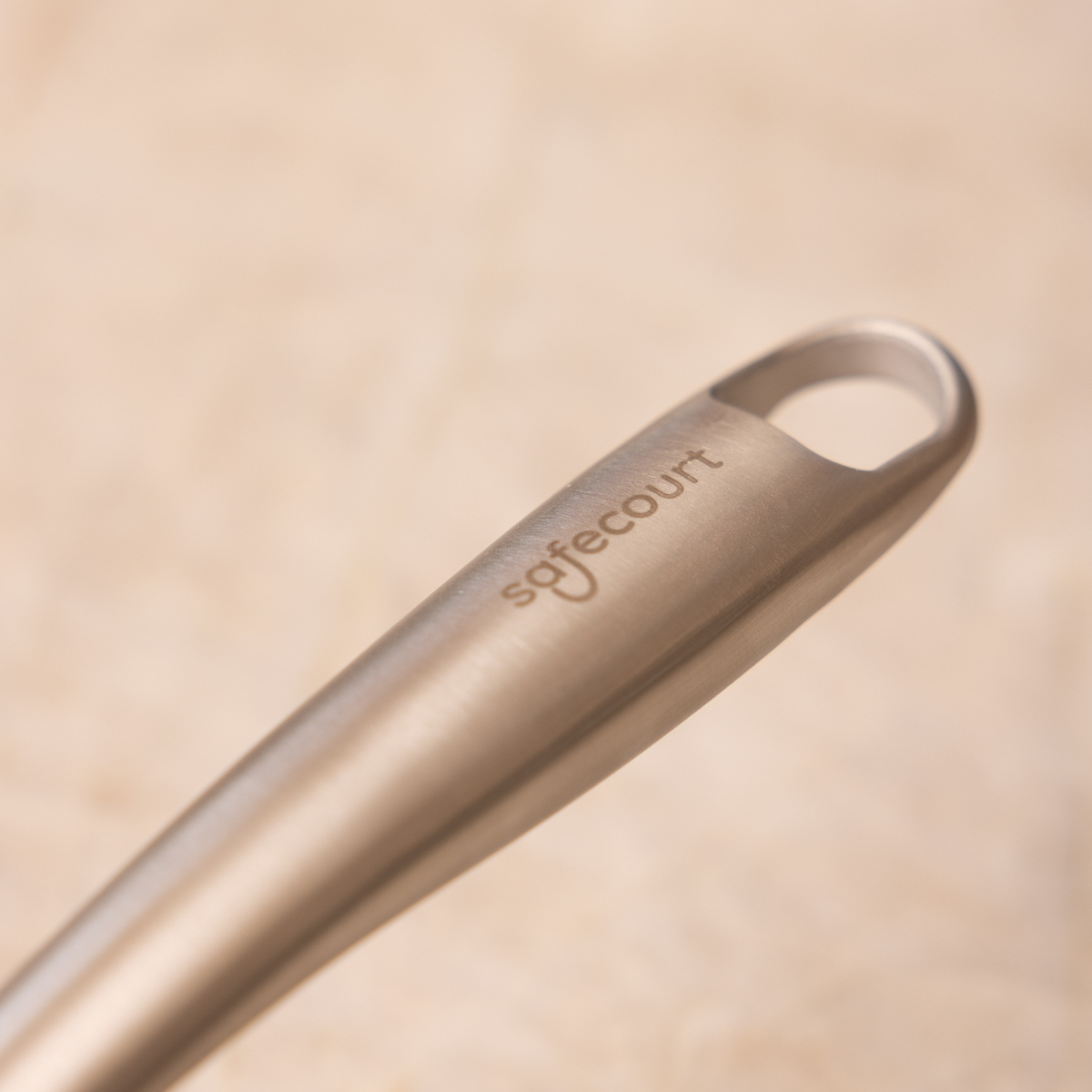 Close-up of a metal handle. The word 'safecourt' is engraved on the handle. The background is blurred, with a light brown tone.