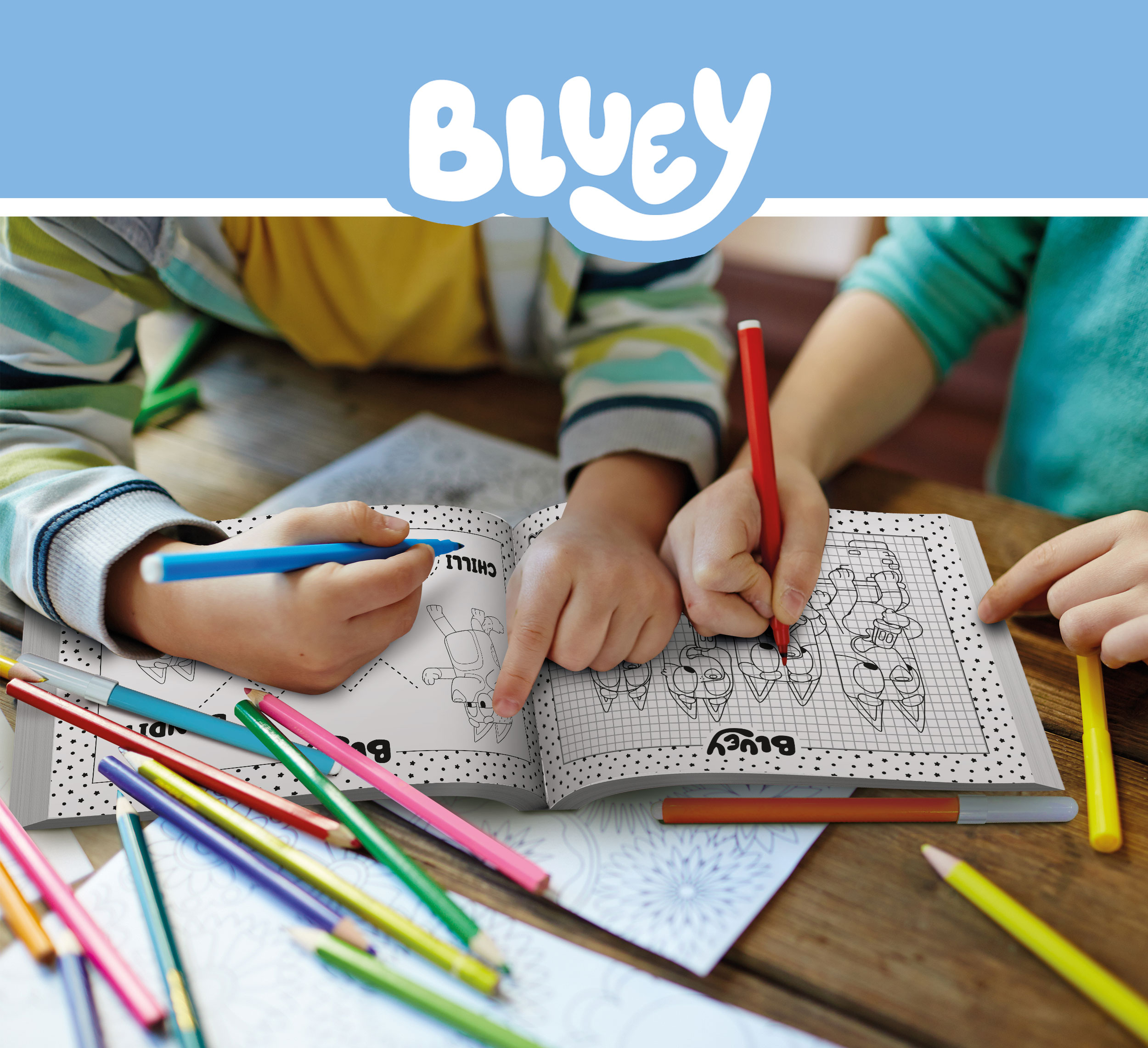 Kinderen kleuren in een Bluey-boek met blauwe en rode stiften, omringd door kleurpotloden op een houten tafel.