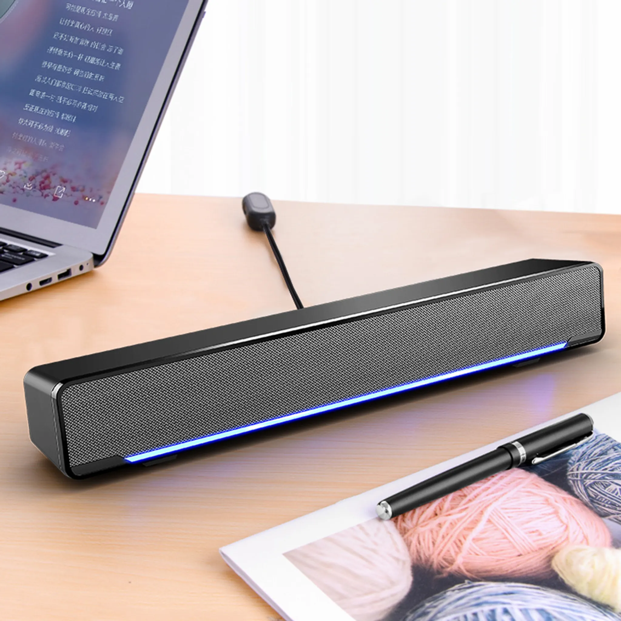 Ein schwarzer Soundbar mit blauem Licht steht auf einem Schreibtisch. Ein Laptop, Stift und Garn sind ebenfalls sichtbar.