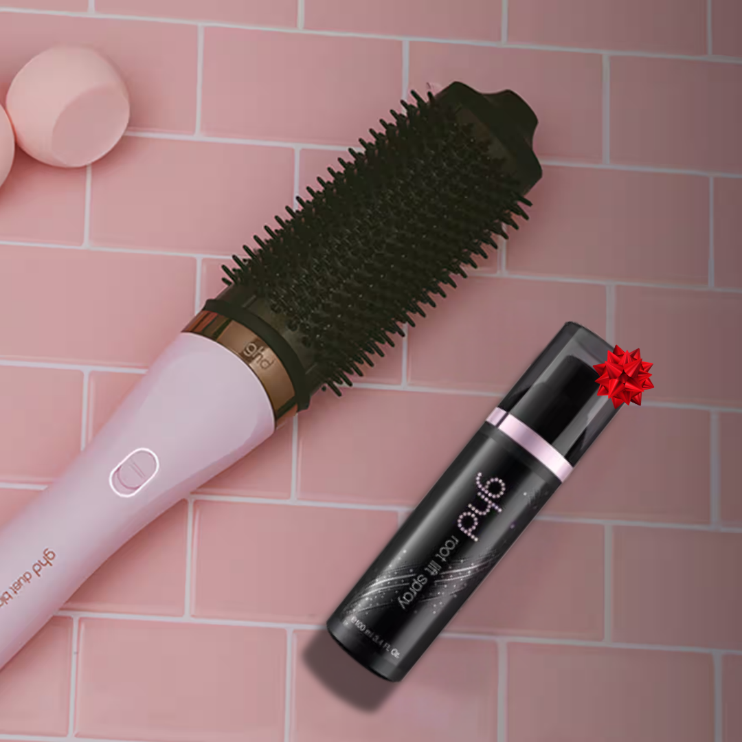 Eine pinke Haarbürste und ein schwarzes ghd Root-Lift-Spray auf einem pinkfarbenen Fliesenuntergrund mit roter Schleife.