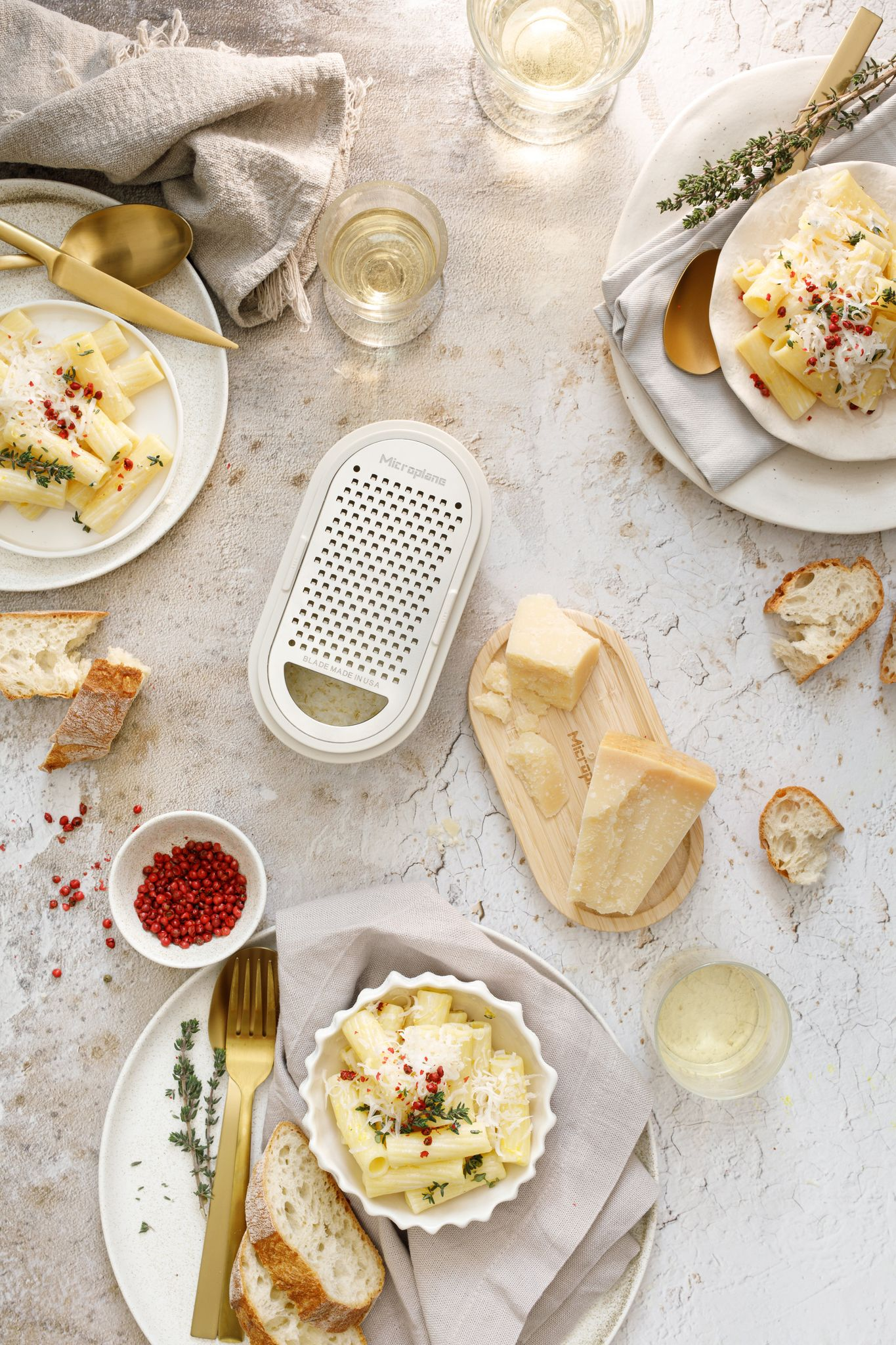 Draufsicht auf Pastagerichte, Käse, Brot und Wein. Ein Reibeisen und rosa Pfeffer sind ebenfalls vorhanden. Gut beleuchtet und appetitlich.