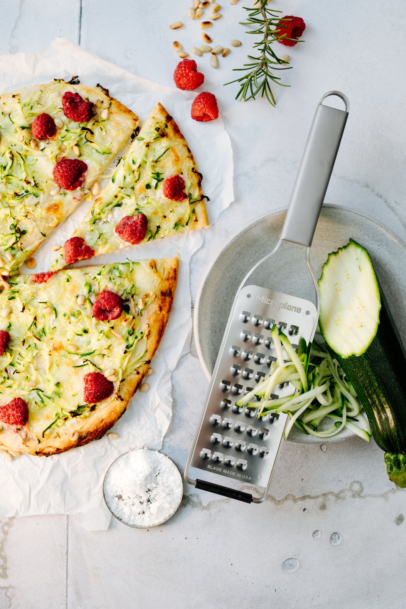 Pizzaschnitten mit Himbeeren und Zucchini. Reibe, Zucchinihälfte, Pinienkerne und Salz. Weißer Hintergrund.