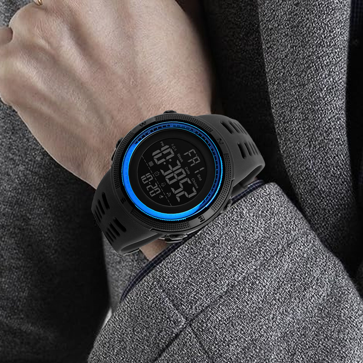 Eine Person trägt eine schwarze Digitaluhr mit blauem Rahmen. Die Uhr zeigt die Zeit und das Datum an. Die Person trägt einen grauen Anzug.