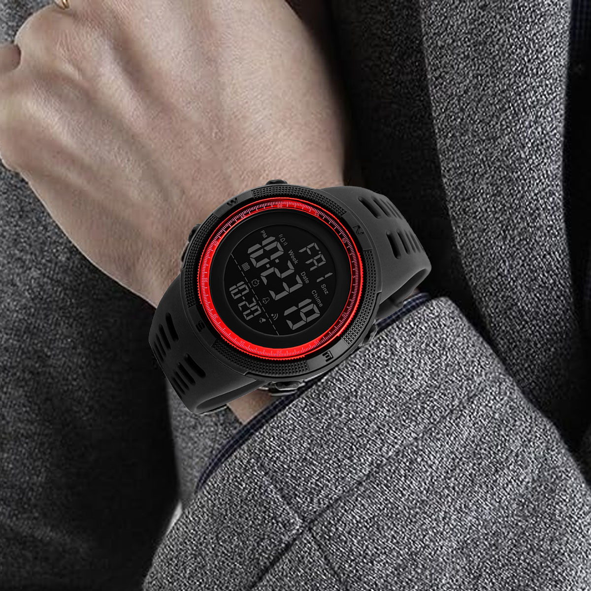 Eine Person trägt eine schwarze Digitaluhr mit roter Lünette. Die Uhr zeigt die Uhrzeit an. Die Person trägt einen grauen Anzug.