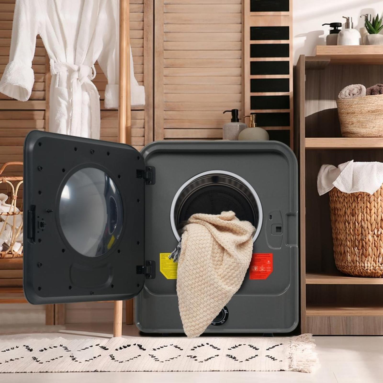Ein grauer Trockner mit offener Tür enthält eine beige Decke. Ein weißer Bademantel hängt in der Nähe. Regale halten Körbe und Toilettenartikel.