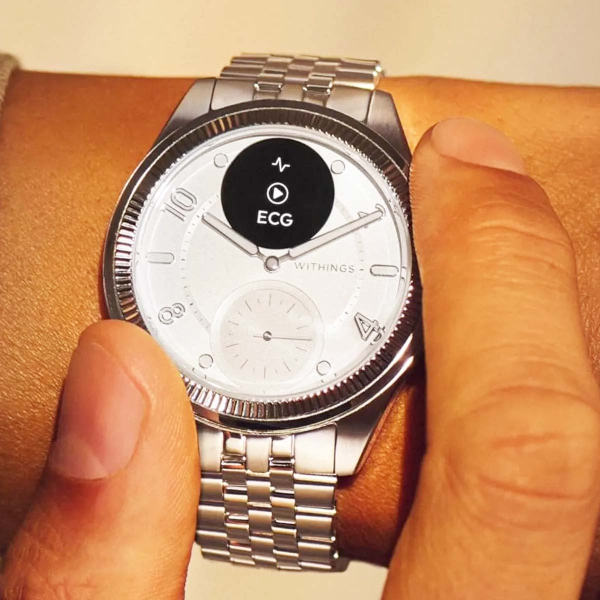 Srebrny zegarek na rękę wyświetlający odczyt EKG. Palec dotyka tarczy zegarka. Zegarek jest na nadgarstku osoby.