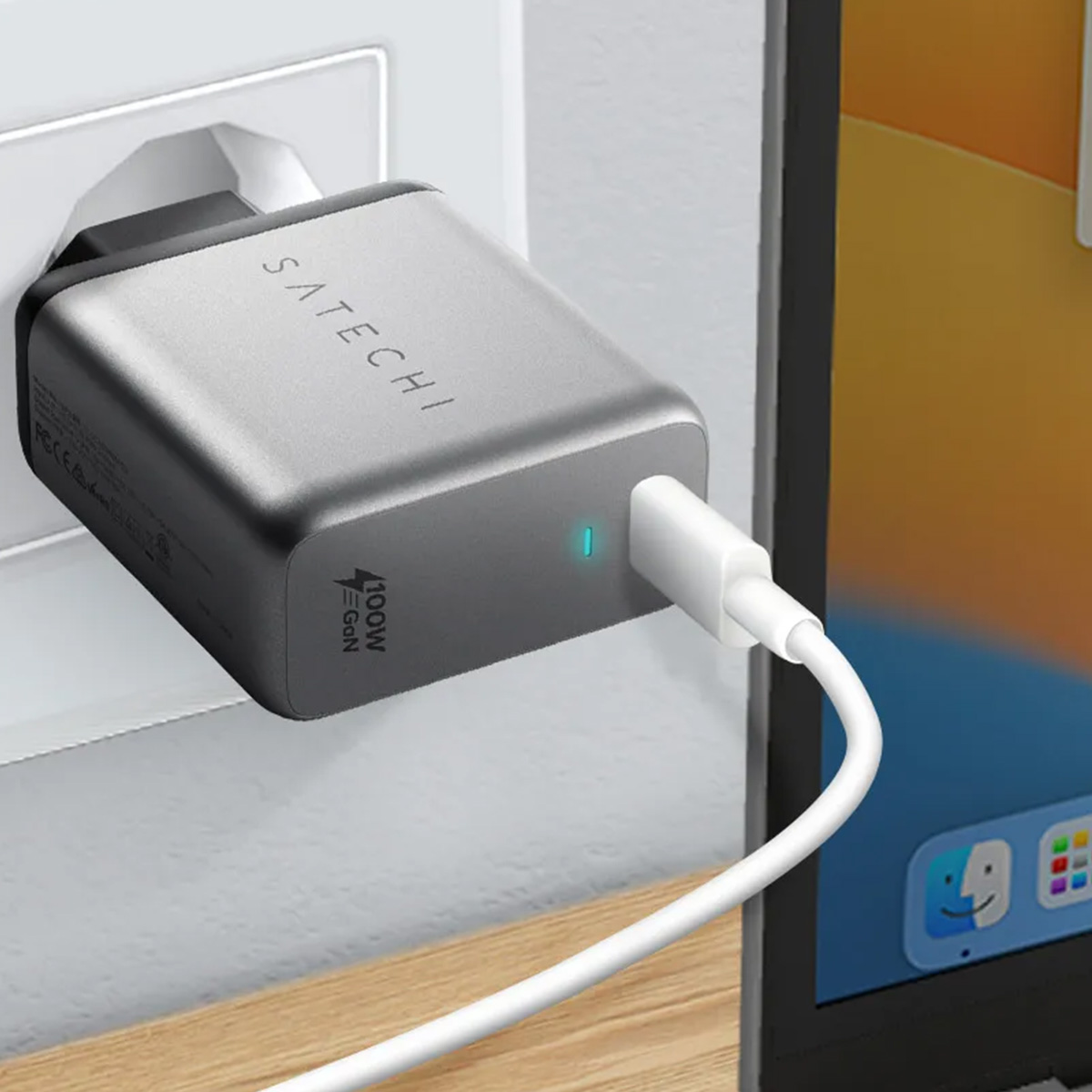 Un caricabatterie Satechi 100W GaN argentato collegato a una presa a muro. Un cavo bianco si collega a un laptop.
