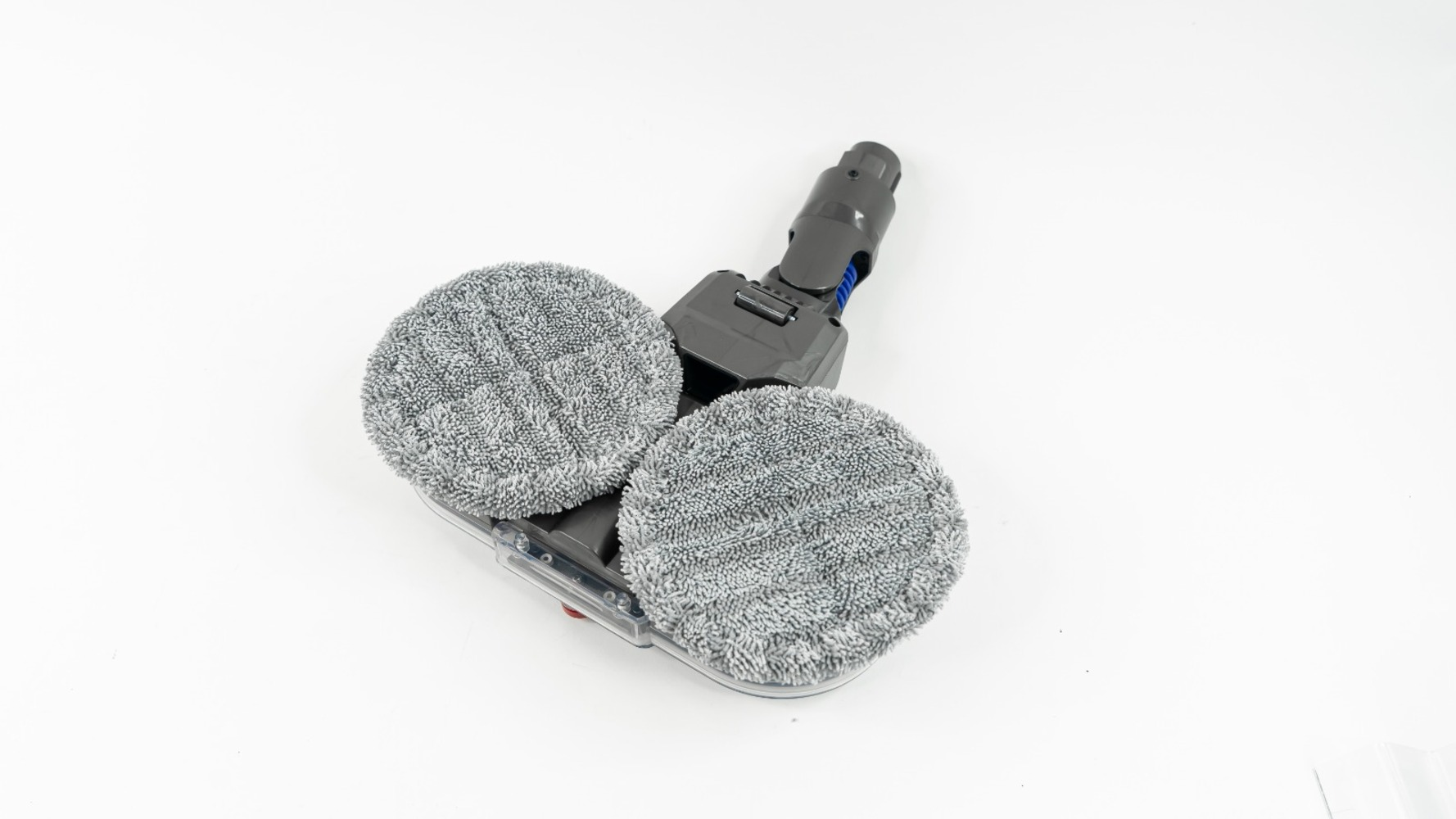Un accesorio de limpieza de suelos gris y negro con dos almohadillas de limpieza redondas sobre una superficie blanca. El accesorio está en ángulo.
