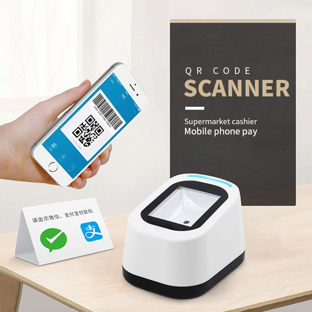 Eine Hand hält ein Telefon mit einem QR-Code. Ein Scanner und ein Schild stehen auf einem Tisch. Das Schild sagt 'QR CODE SCANNER'.