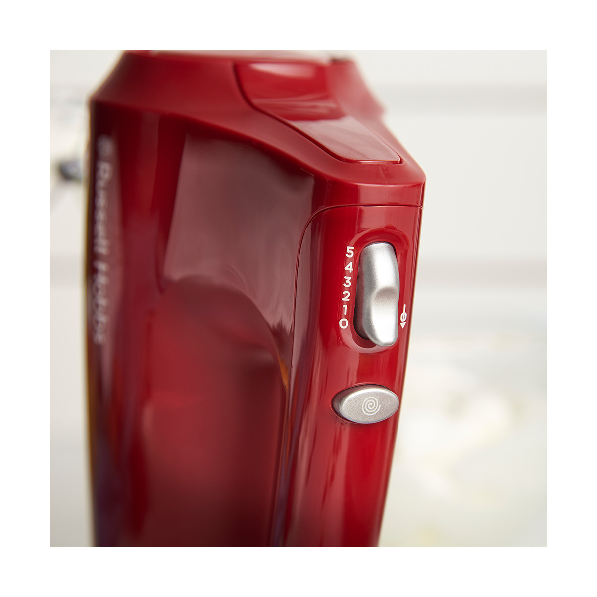 Un primo piano di un mixer a mano rosso. Mostra le impostazioni di velocità, un interruttore argentato e un pulsante di avvio. Lo sfondo è sfocato.