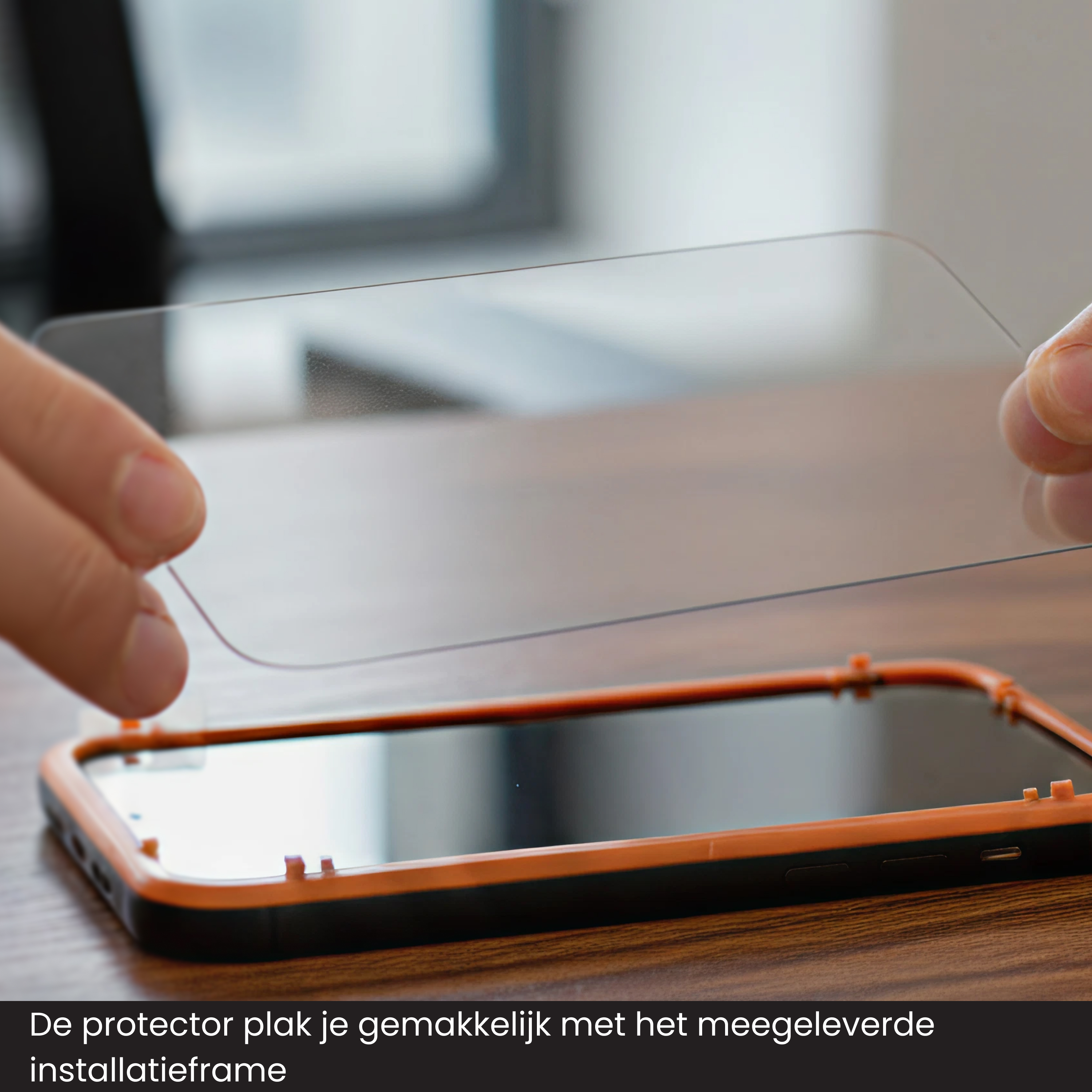 Handen houden een schermbeschermer boven een telefoon met een oranje frame. De beschermer is transparant.