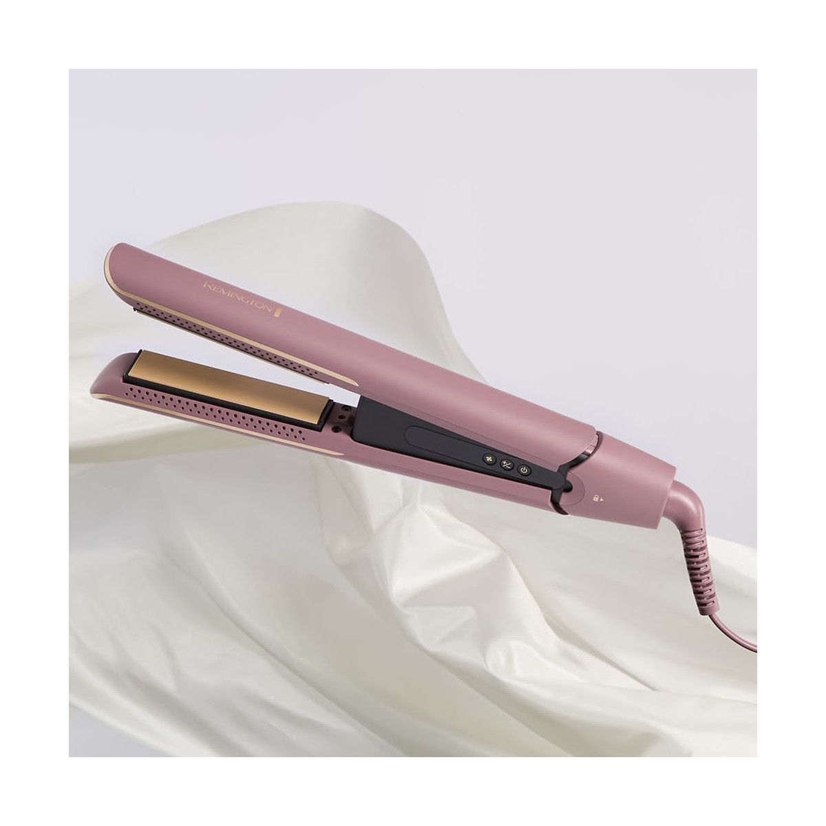 Una piastra per capelli Remington rosa è appoggiata aperta su un tessuto bianco drappeggiato. La piastra ha piastre dorate e un pannello di controllo nero.