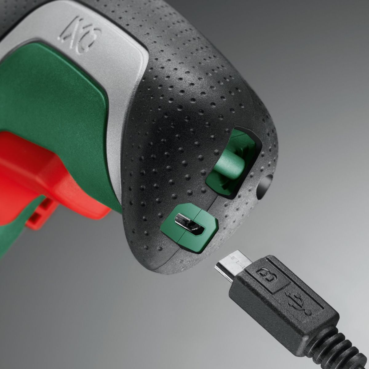 Ein schwarzes und grünes Elektrowerkzeug ist mit einem USB-Kabel verbunden. Das Werkzeug hat einen roten Auslöser, und das USB-Kabel ist eingesteckt.