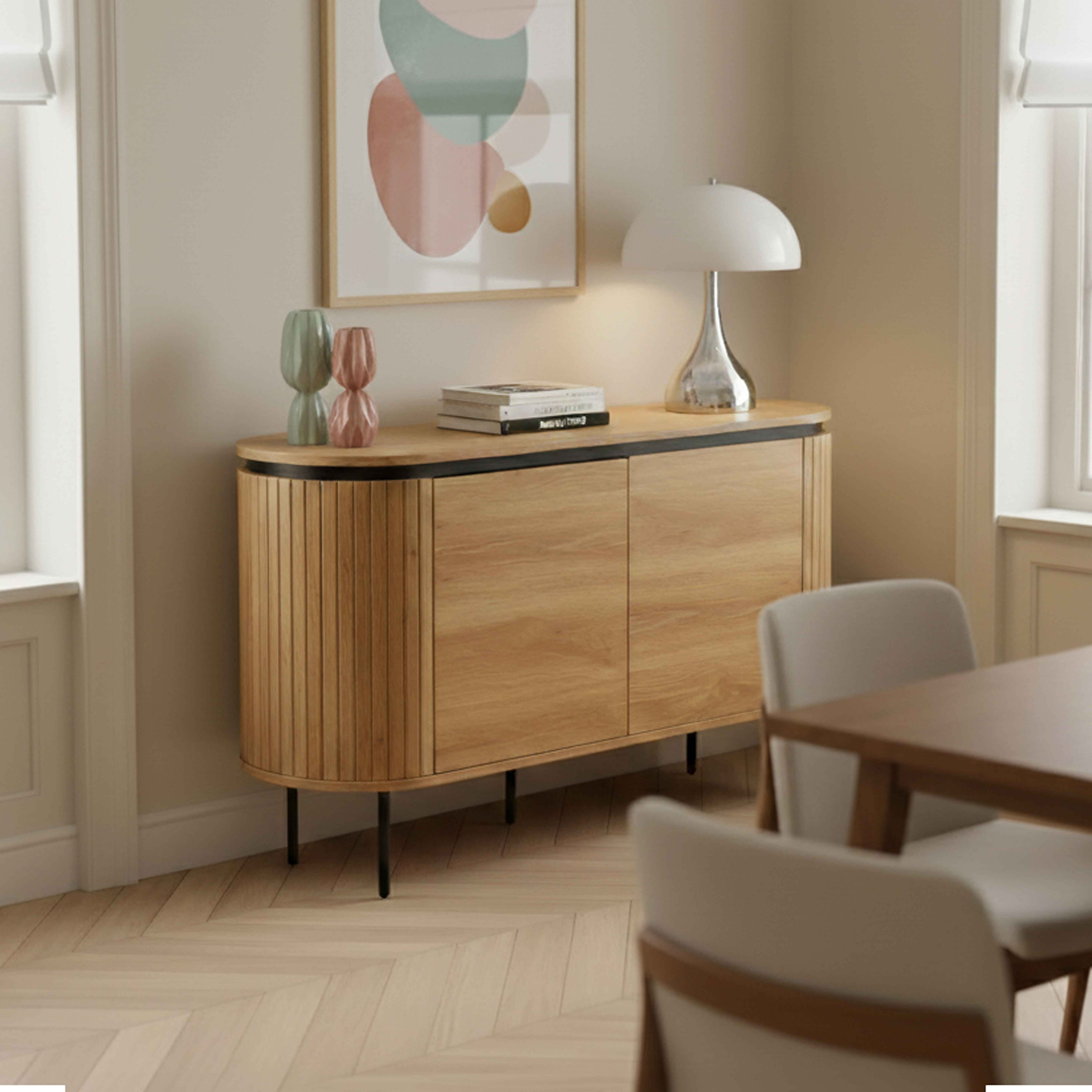 Ein Holzschrank mit einer Lampe, Kunst an der Wand und Stühlen davor.