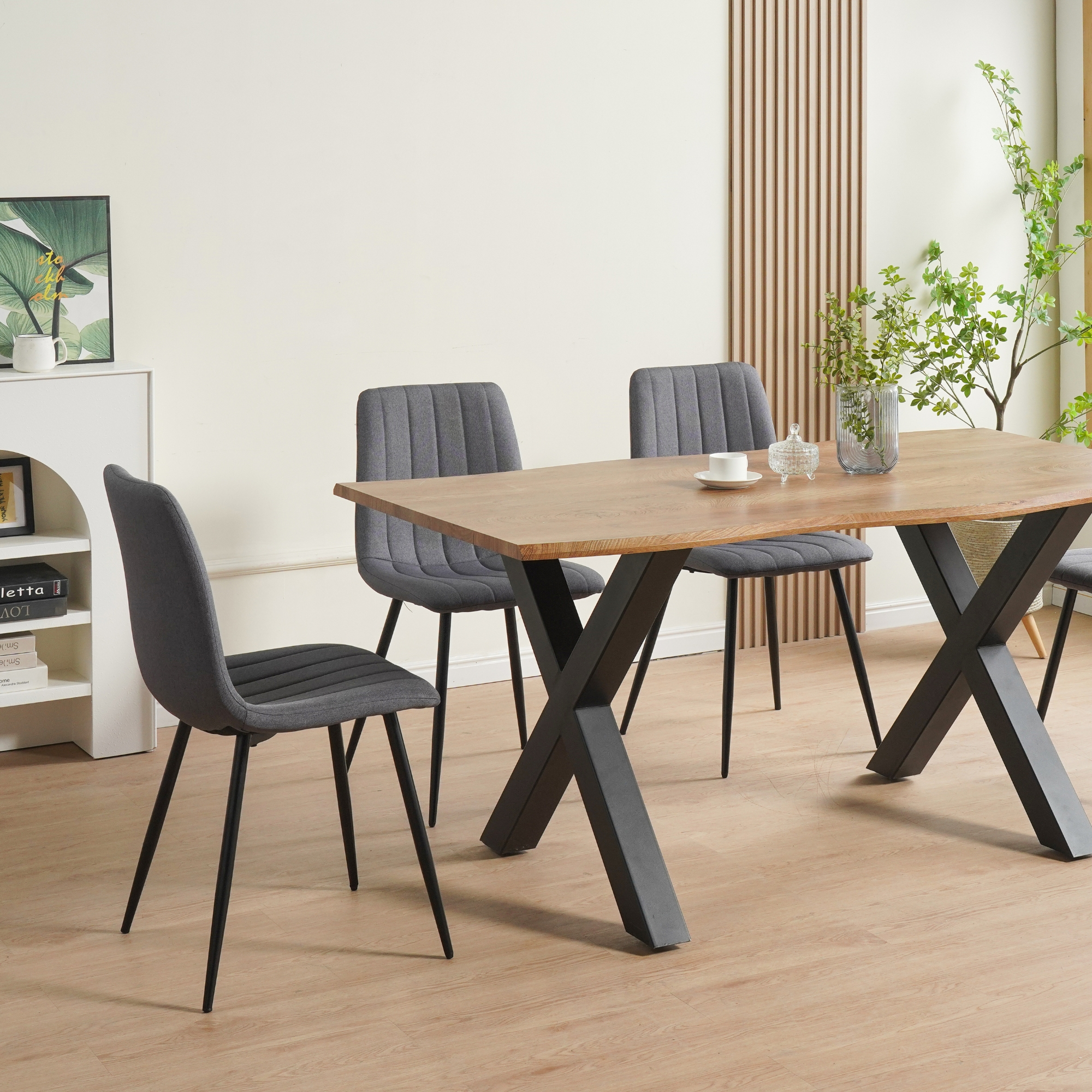 Ein Holztisch mit schwarzen Beinen und grauen Stühlen in einem Raum. Im Hintergrund befinden sich eine Pflanze und ein Kunstwerk.
