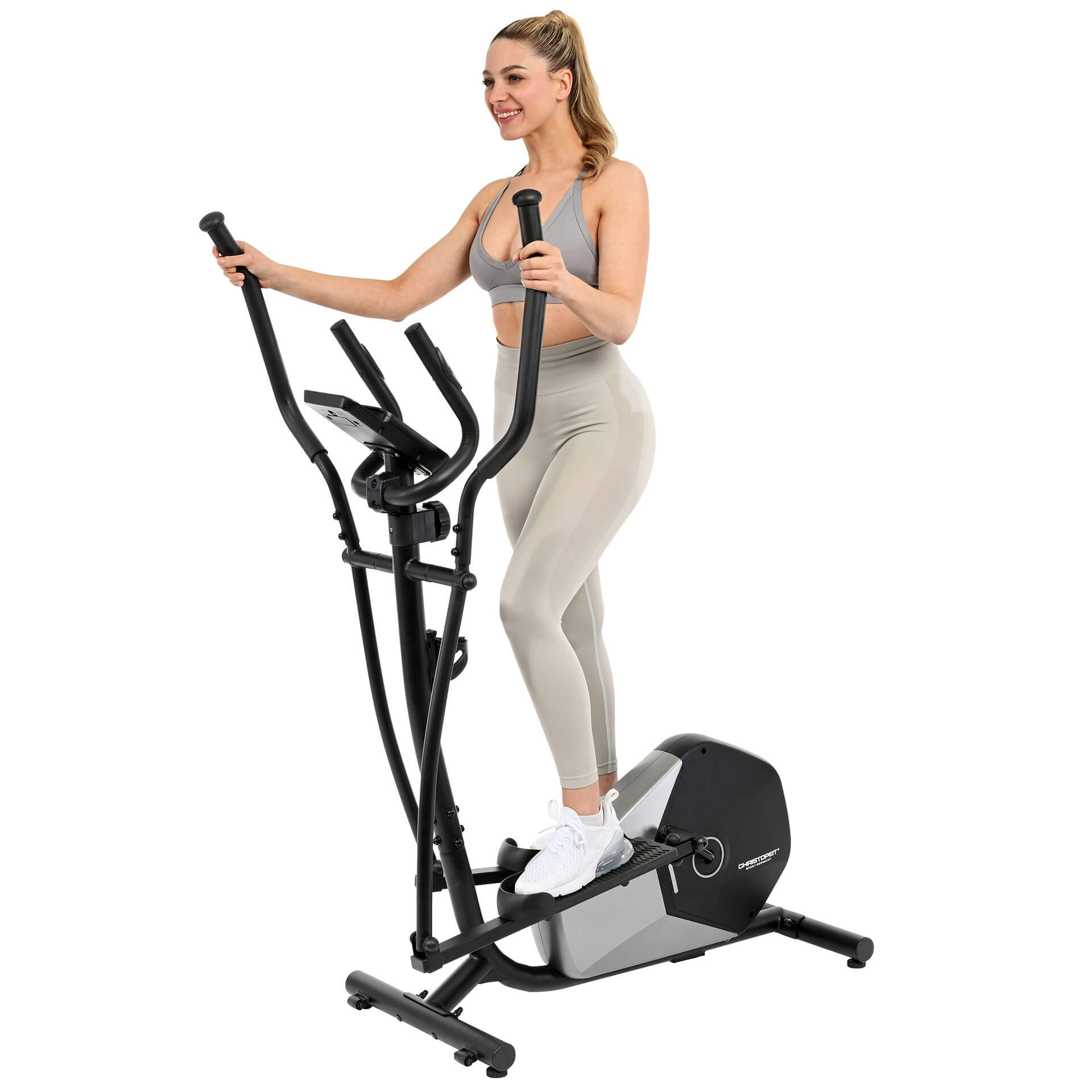 Eine Frau in Sportkleidung trainiert auf einem Crosstrainer. Sie lächelt. Die Maschine ist schwarz und grau, vor weißem Hintergrund.