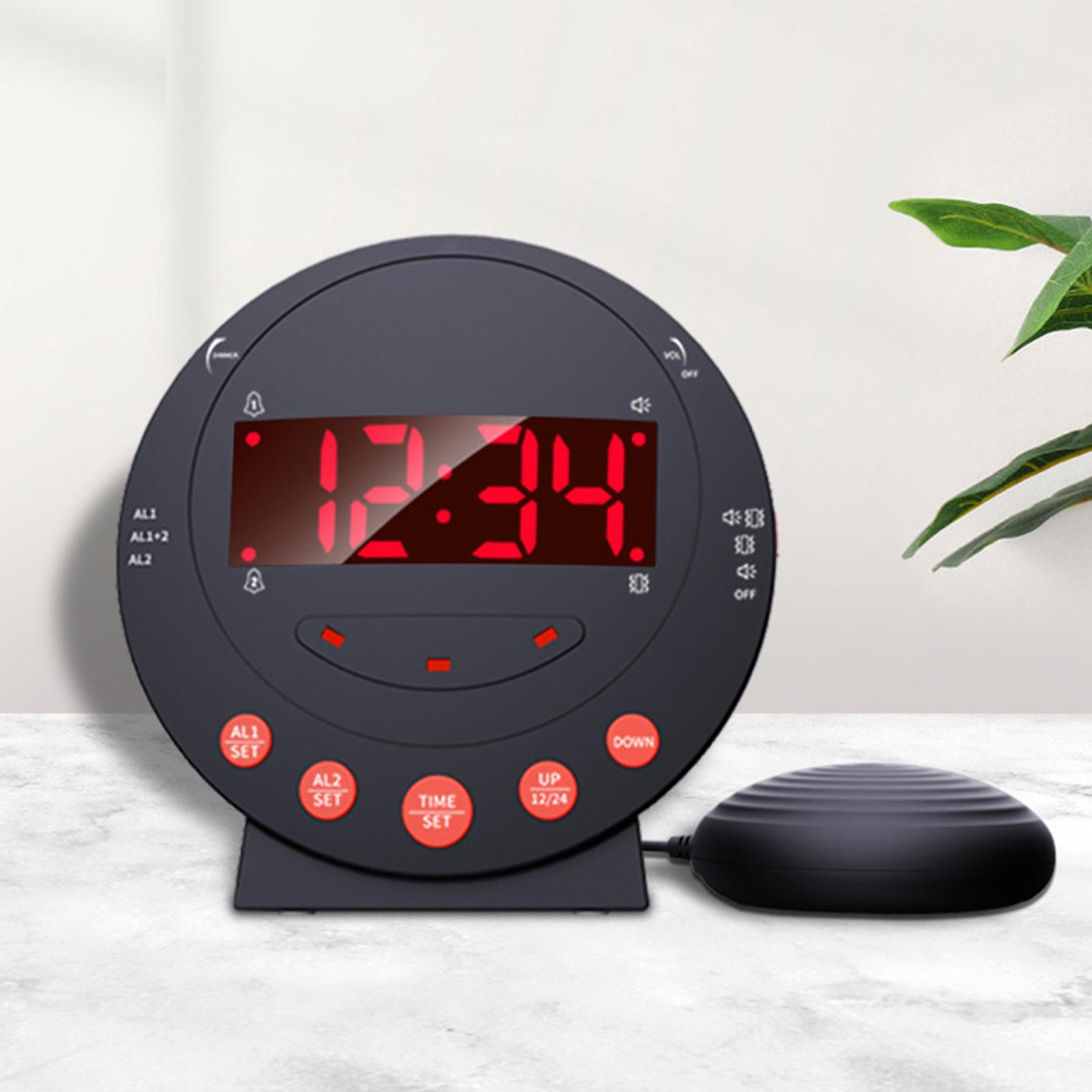 Ein schwarzer digitaler Wecker zeigt 12:34 an. Er hat rote Knöpfe und ein angeschlossenes Vibrationspad.