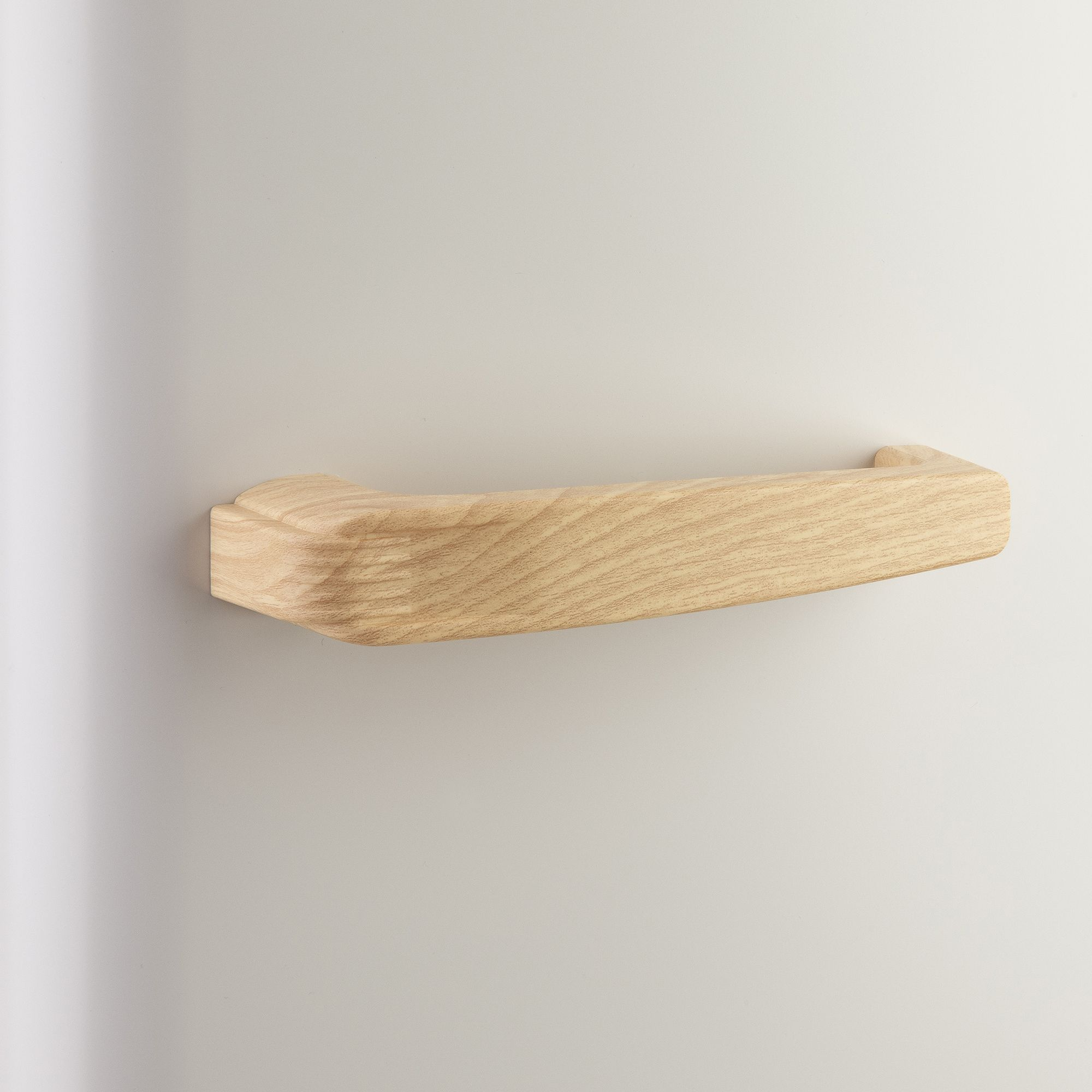 Una maniglia di legno è montata su una parete bianca. La maniglia è marrone chiaro e ha una forma curva.