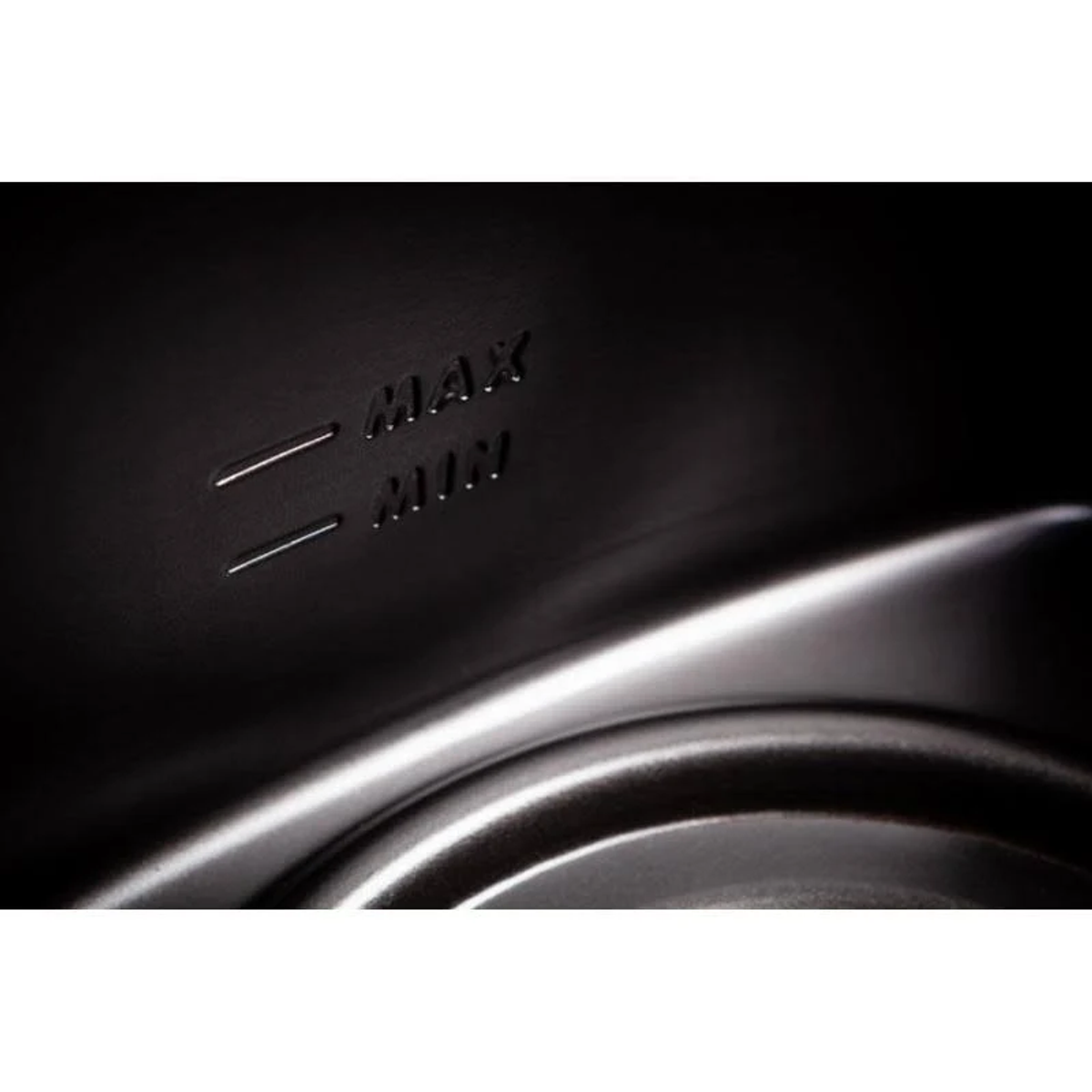 Zbliżenie ciemnego wnętrza z oznaczeniami 'MAX' i 'MIN'. Linie wskazują poziomy. Błyszcząca, metaliczna krzywa na pierwszym planie.