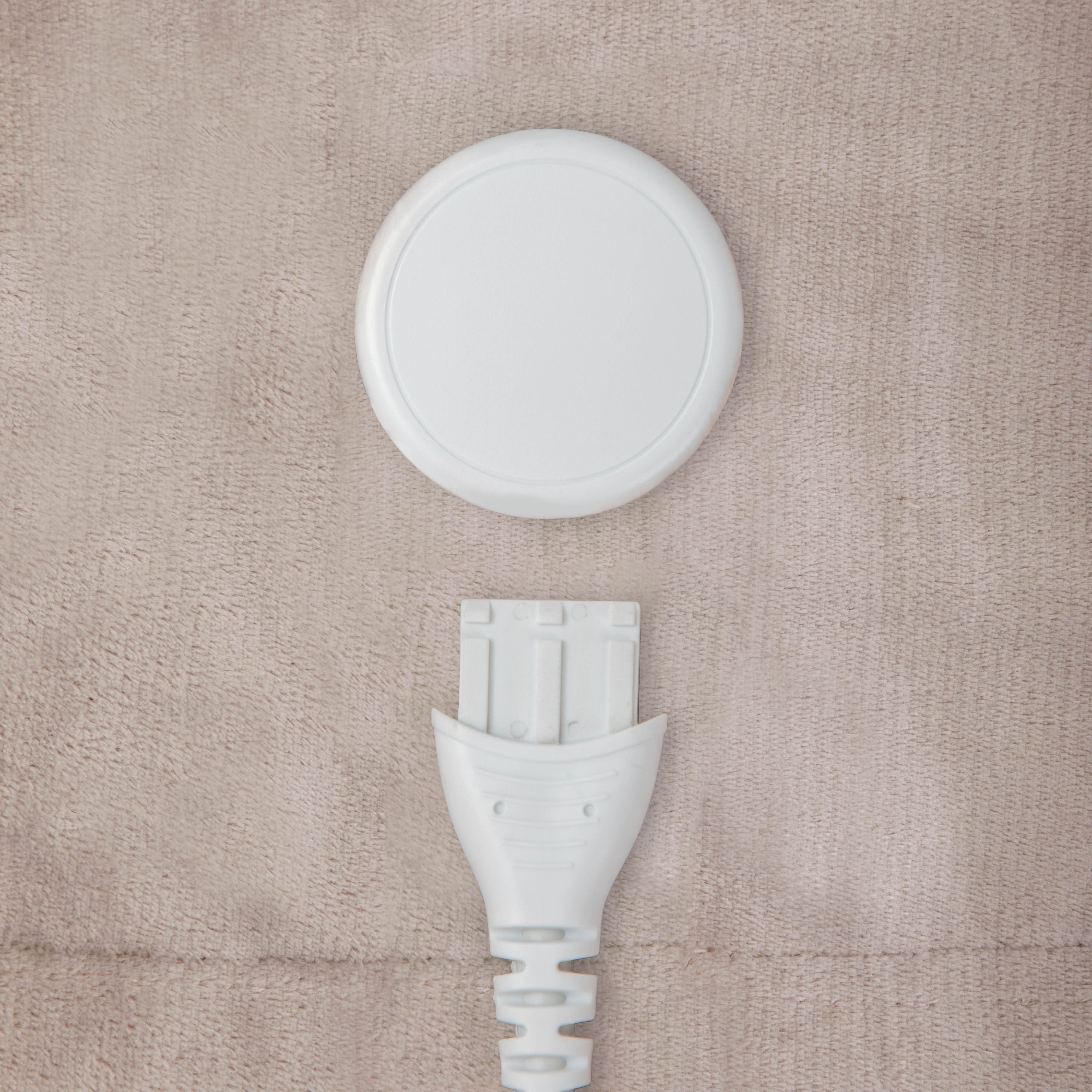 White electric blanket connector and controller on a beige textured surface.