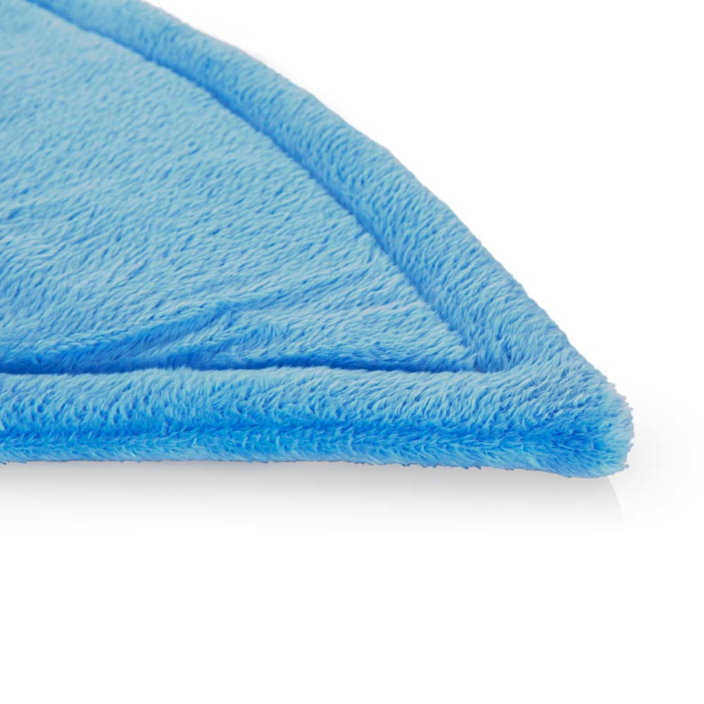 Primer plano de una esquina de manta azul esponjosa. La manta tiene una textura suave y un borde azul más claro. Fondo blanco.